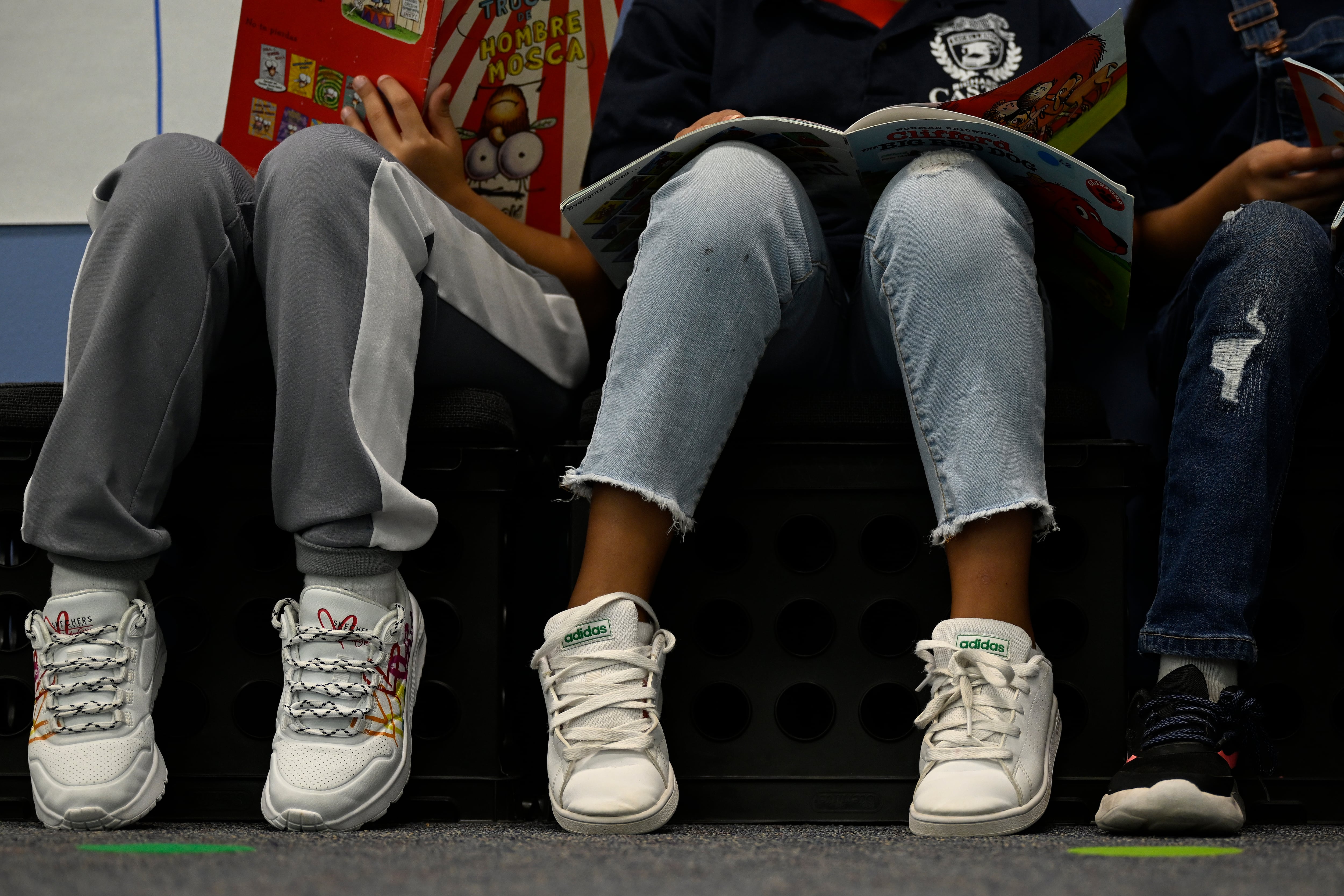 Three students sit side by side and read books. The photo shows just their legs and their sneakers.