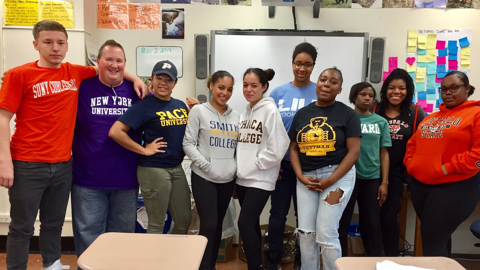 Steven Serling, wearing a New York University shirt, poses with seniors wearing gear to represent the colleges they've committed to attending.