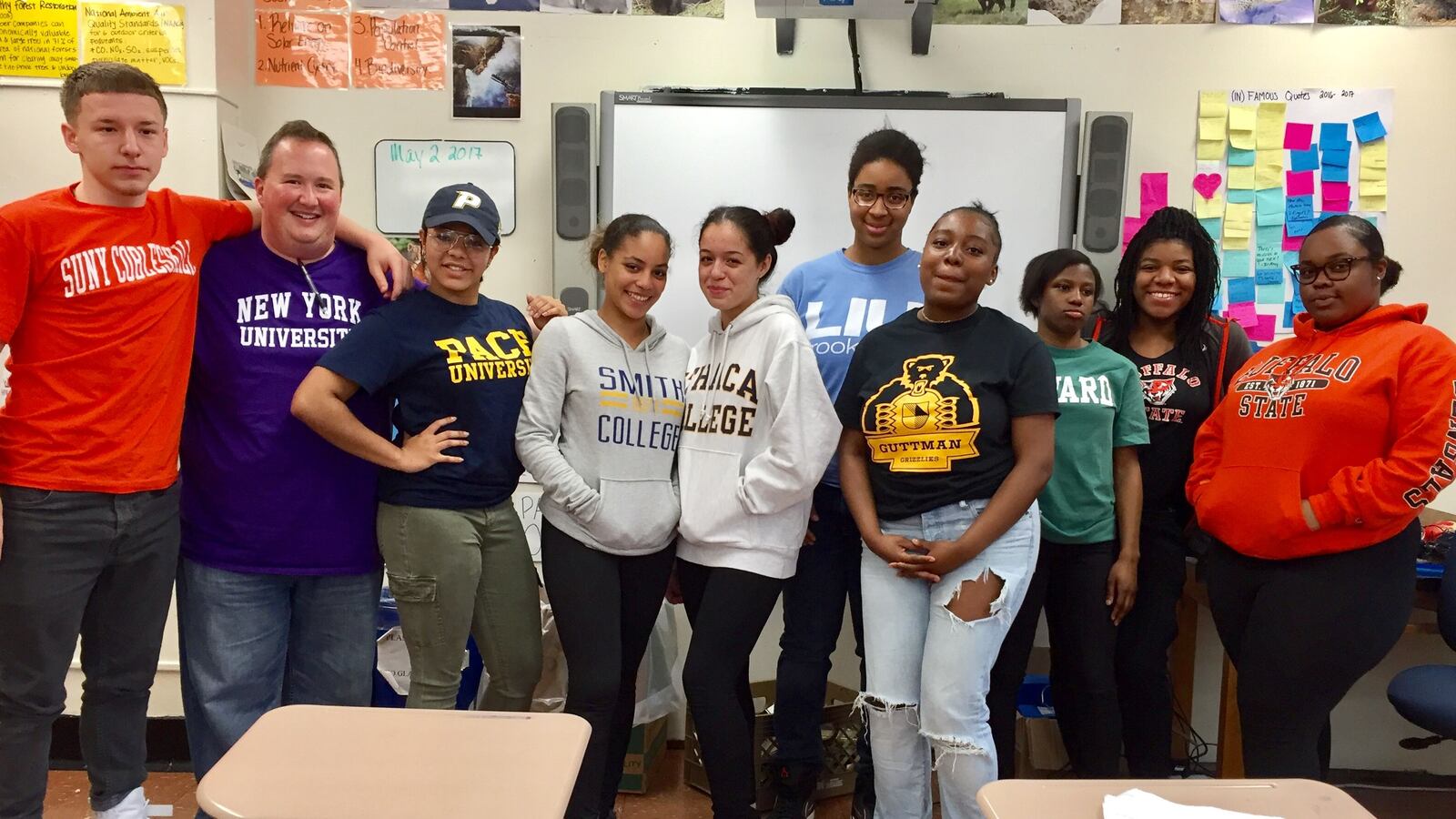 Steven Serling, wearing a New York University shirt, poses with seniors wearing gear to represent the colleges they've committed to attending.