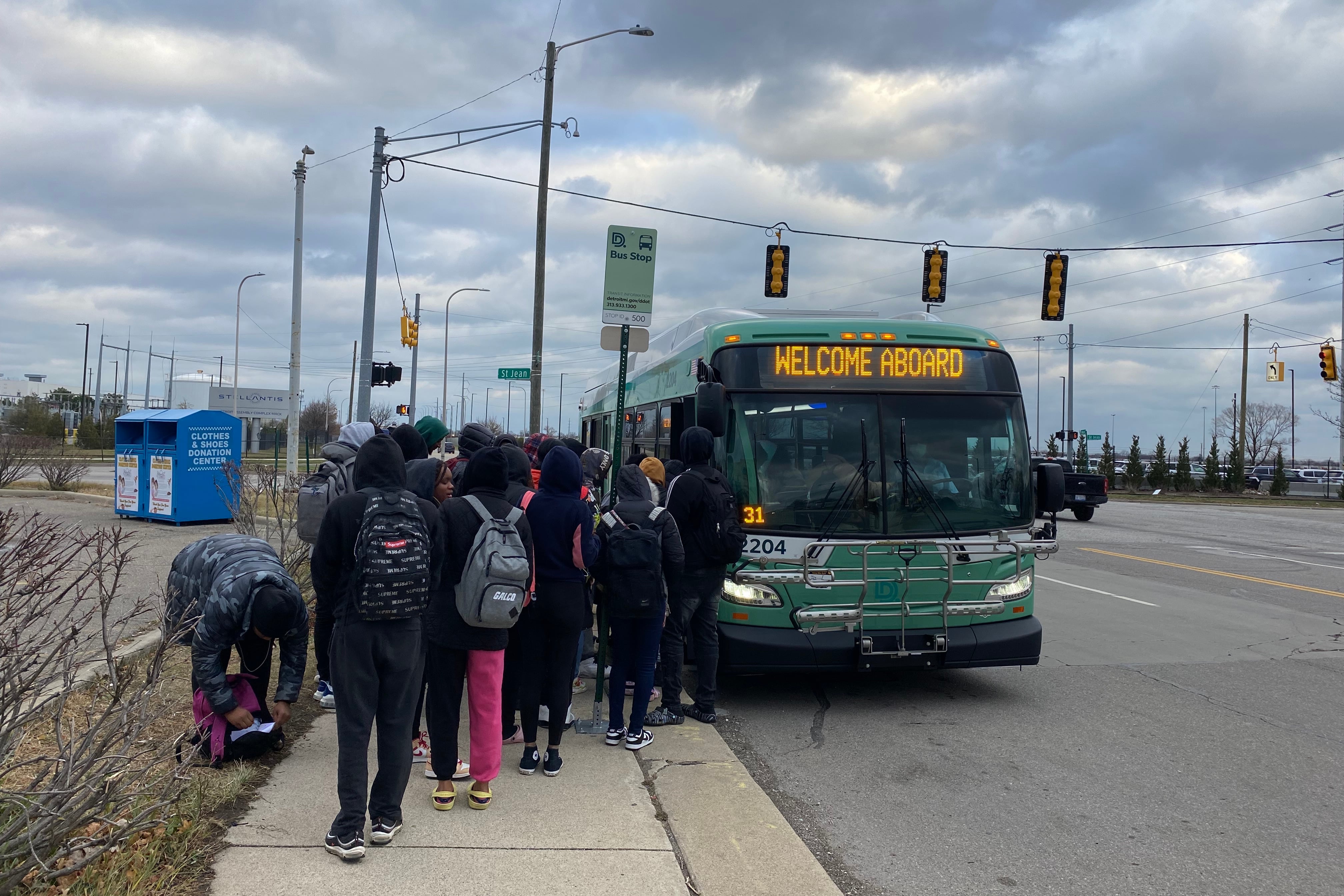 A crowd of students lines up to board a green city bus at a bus stop in Detroit.