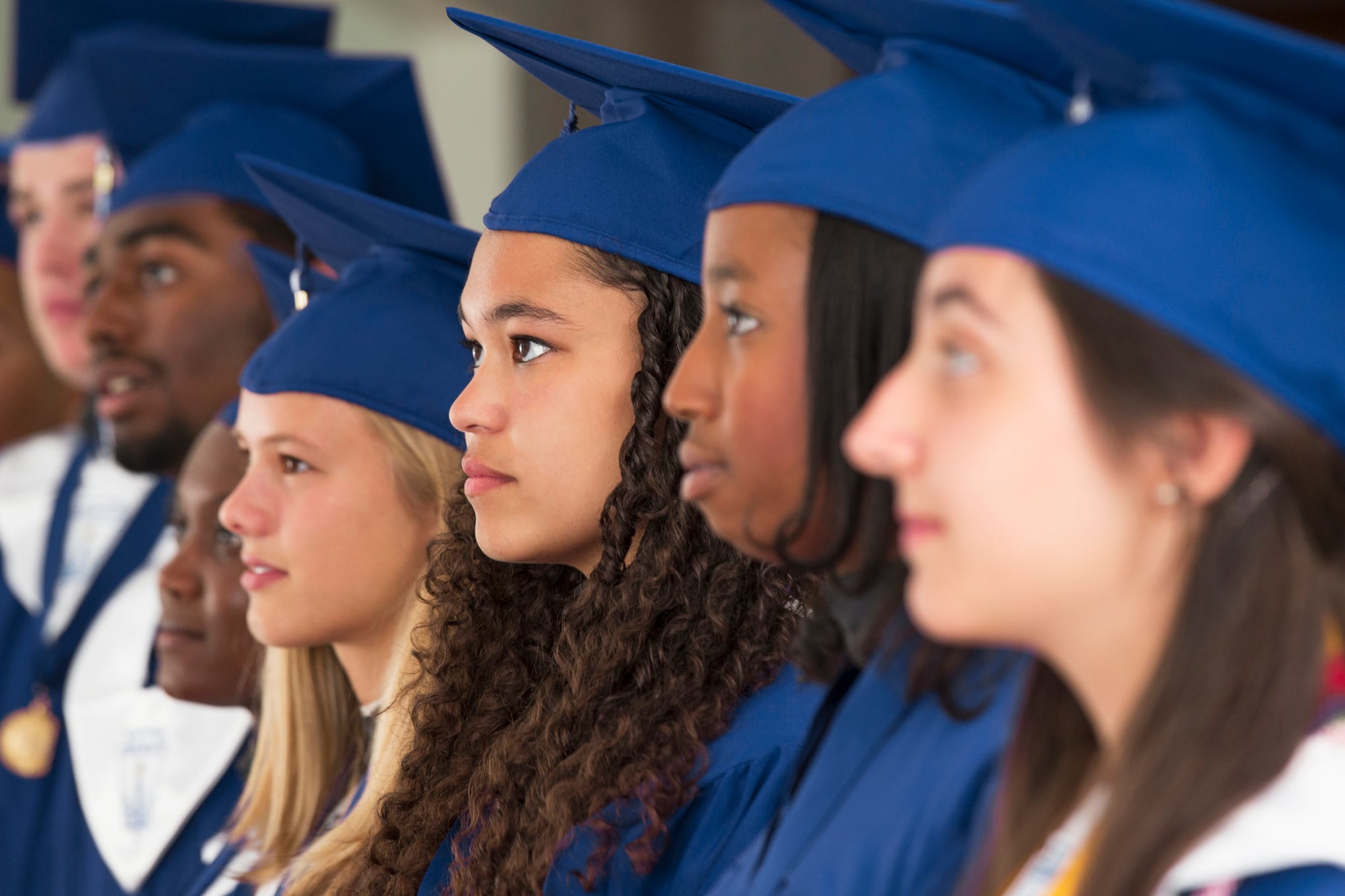 Seven high school students dressed in blue caps and gowns stand for their graduation.