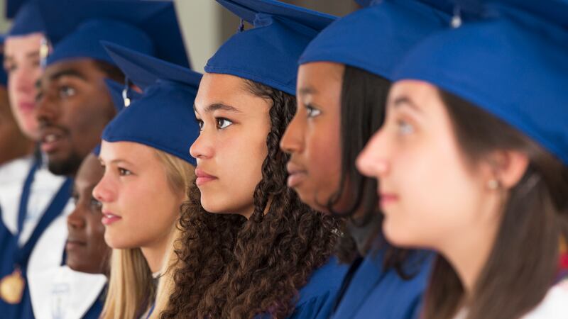 Seven high school students dressed in blue caps and gowns stand for their graduation.