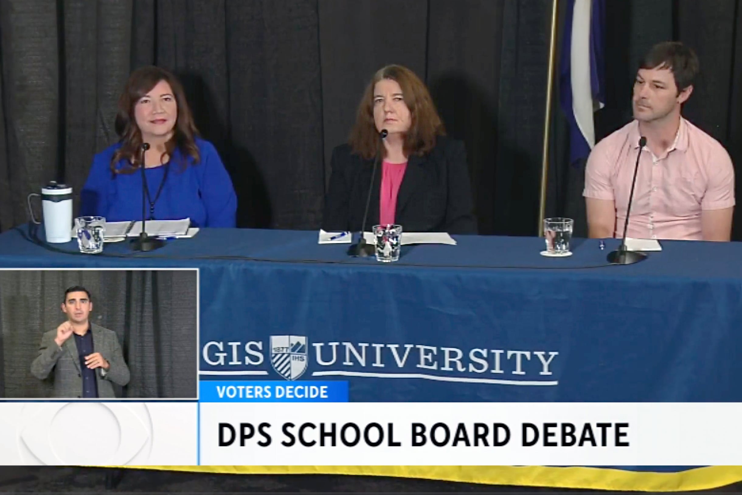 Two women and one man sit behind a table draped in a cloth that says Regis University.