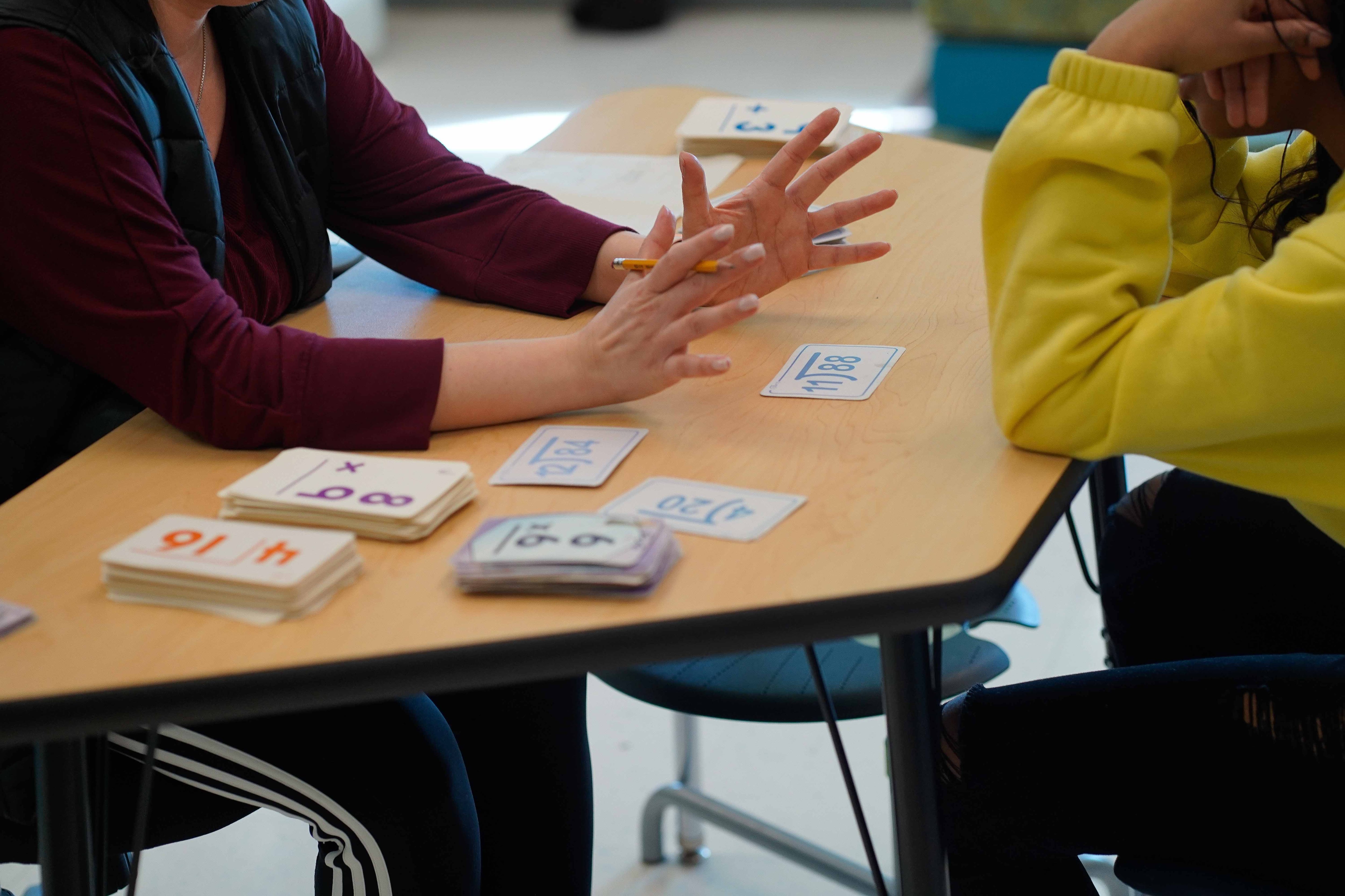 Two people sit at a table working on math flashcards.