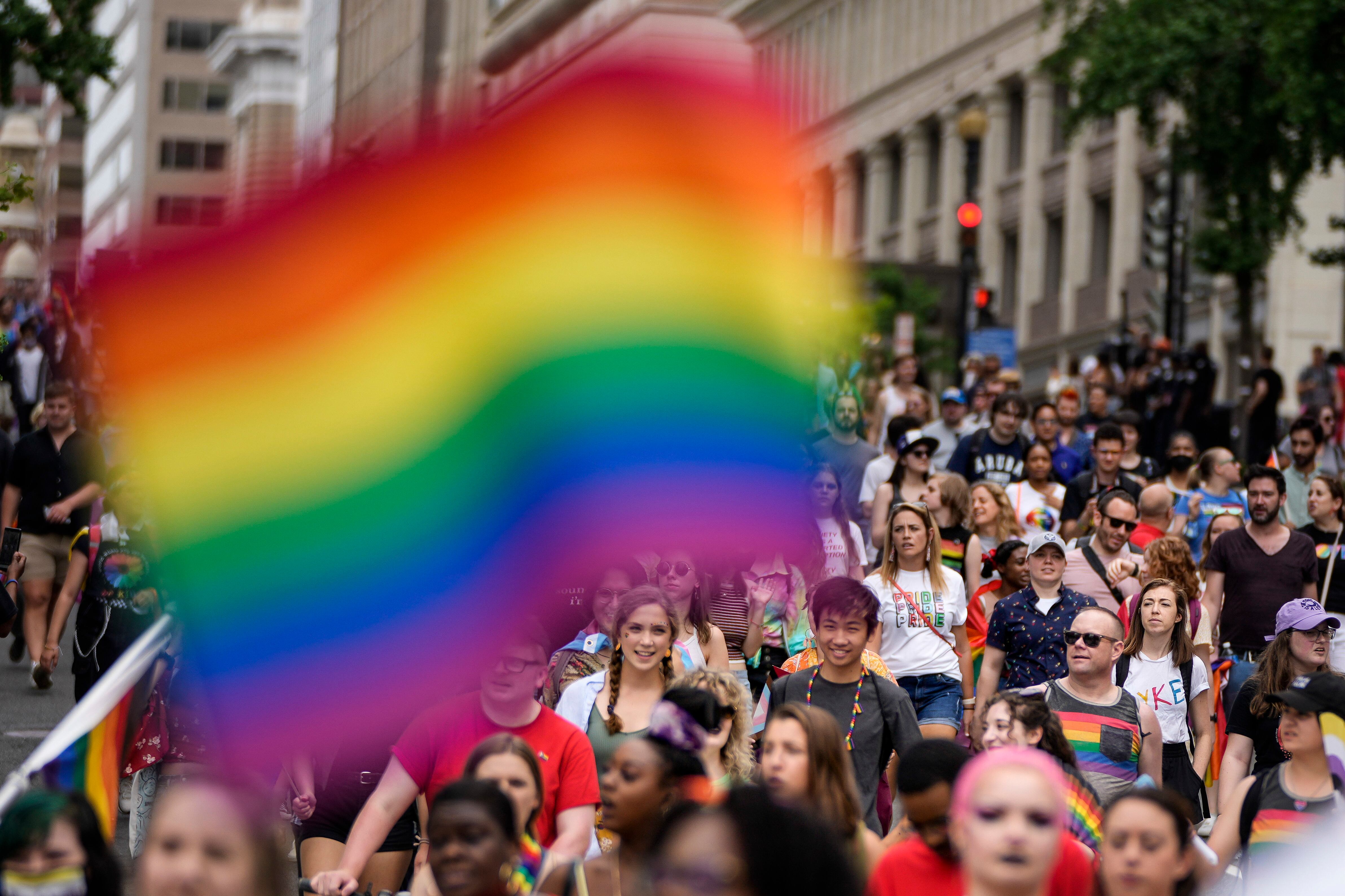 A huge crowd of people march down a city street as a Pride flag hangs in the foreground.