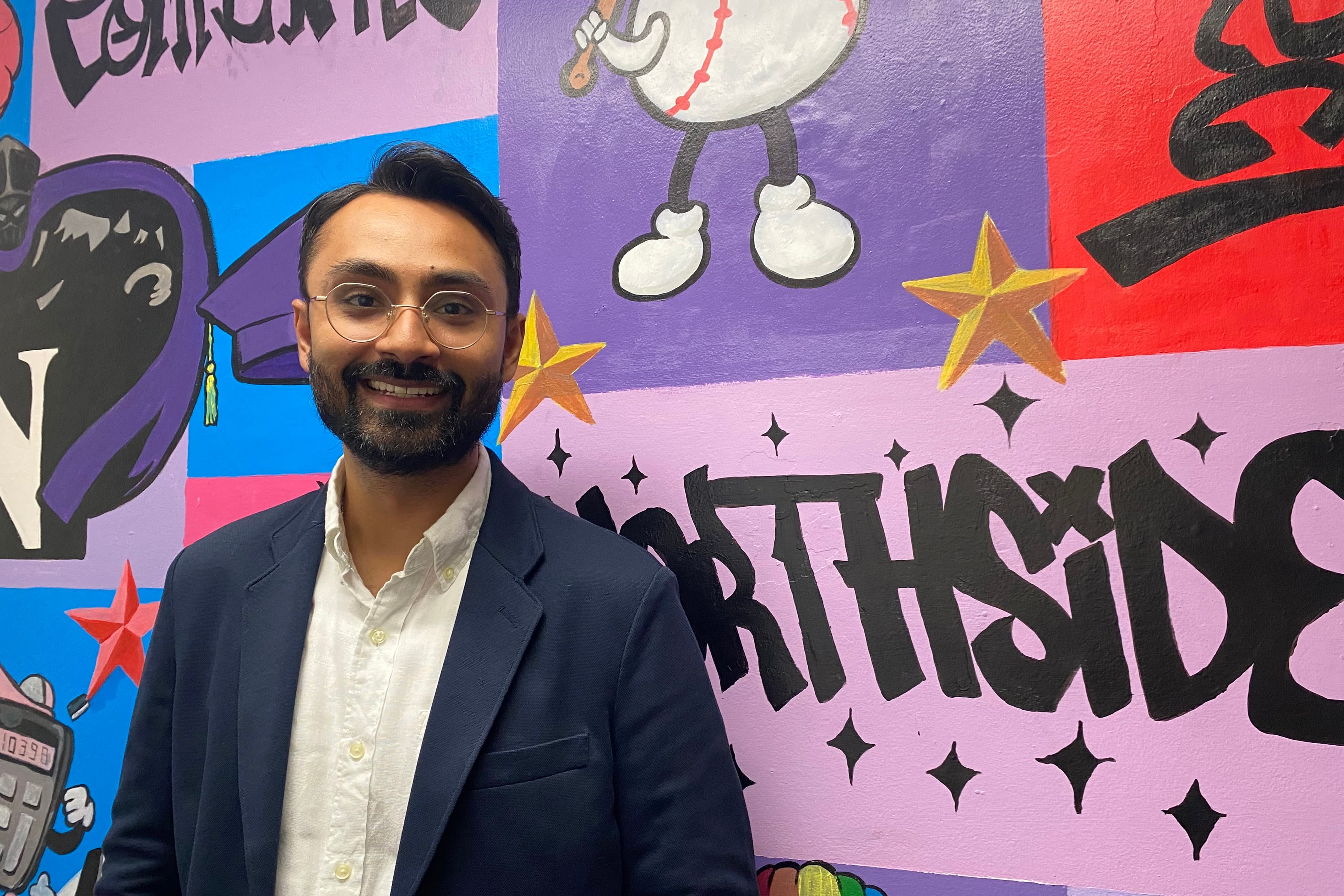 A photograph of a man in a suit posing for a photograph in front of a colorful wall.