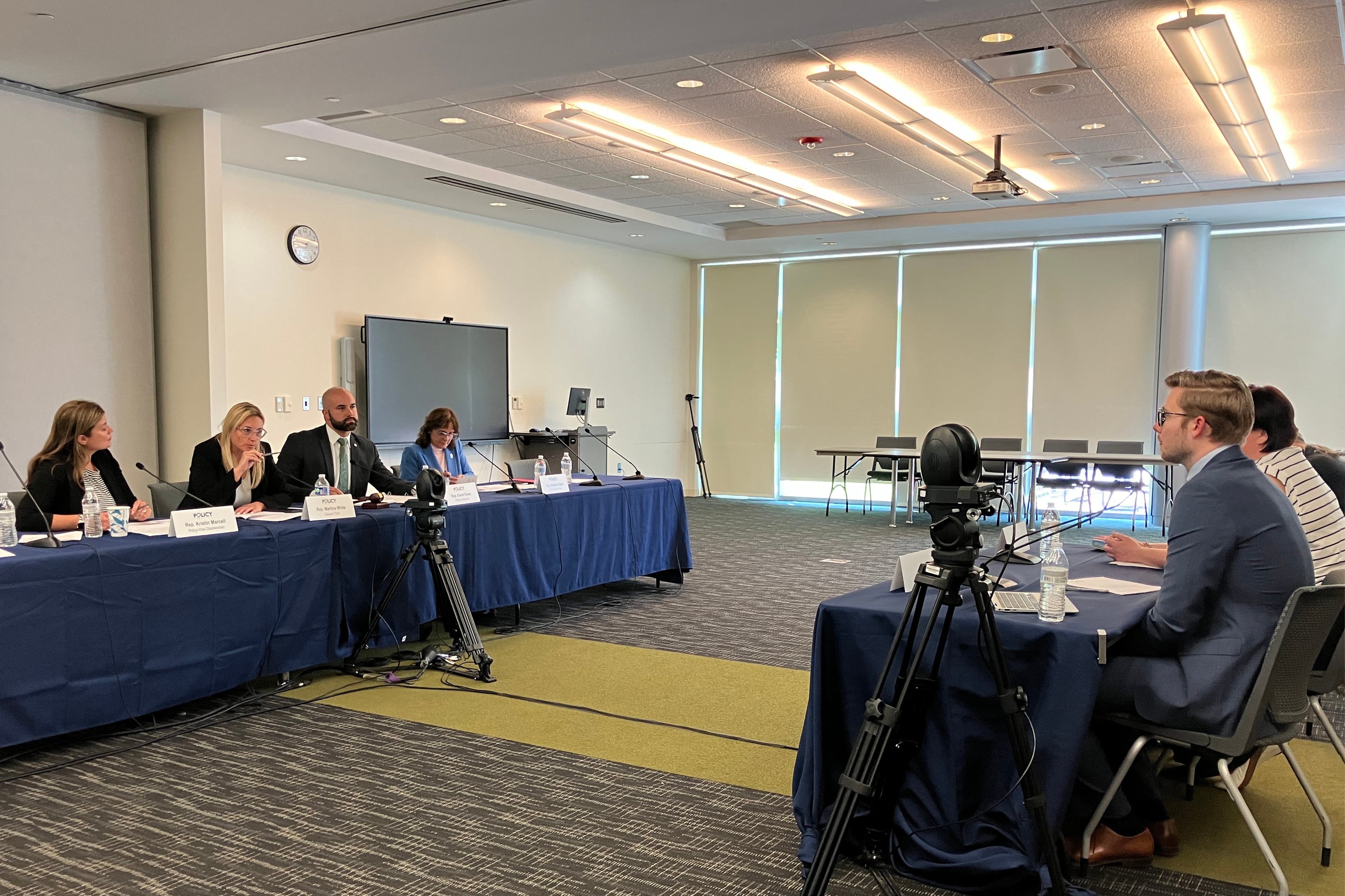 Two tables with a line of people sitting at each table and facing each other in a conference room.