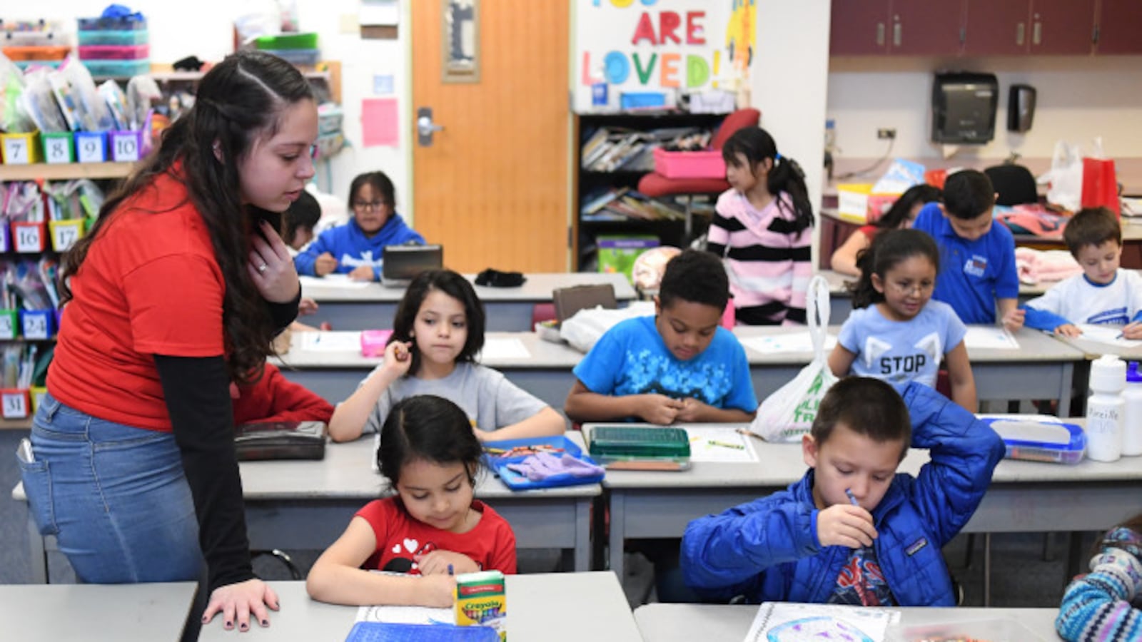 Teacher Hannah Maldonado wears a red T-shirt while looking at first graders doing work at rows of desks at Denver’s Barnum Elementary School in February 2019.