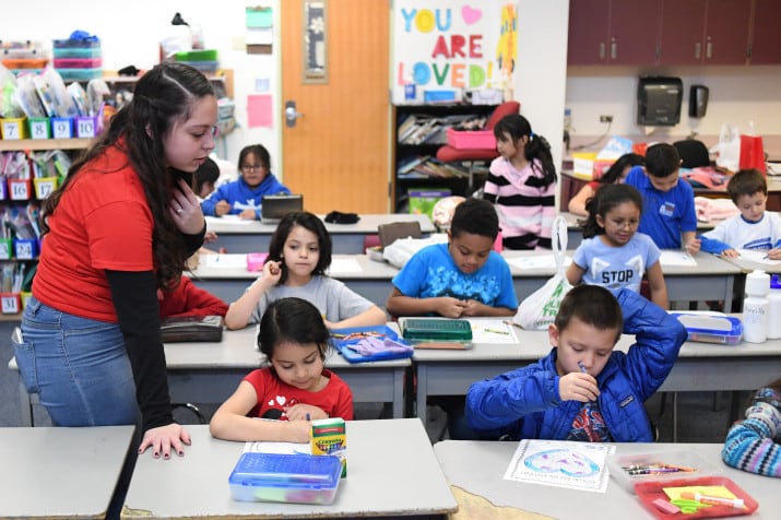 Teacher Hannah Maldonado wears a red T-shirt while looking at first graders doing work at rows of desks at Denver’s Barnum Elementary School in February 2019.
