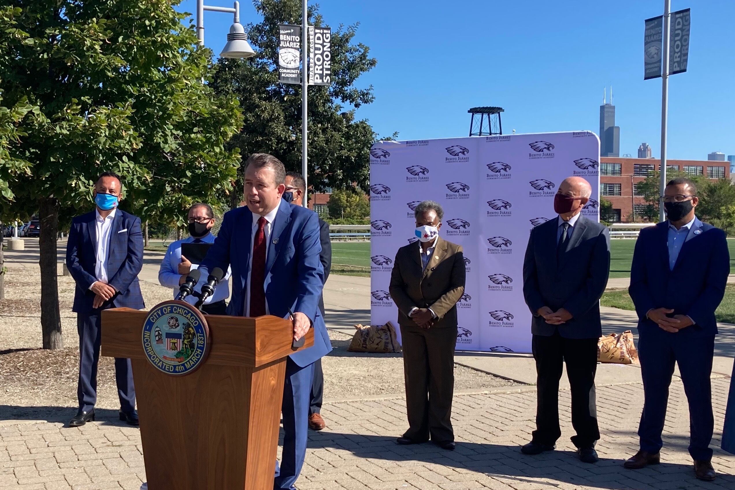 Newly announced Chicago Public Schools CEO Pedro Martinez, wearing a blue suit, stands outside at a lectern and speaks during a press conference as district leaders look on behind him.