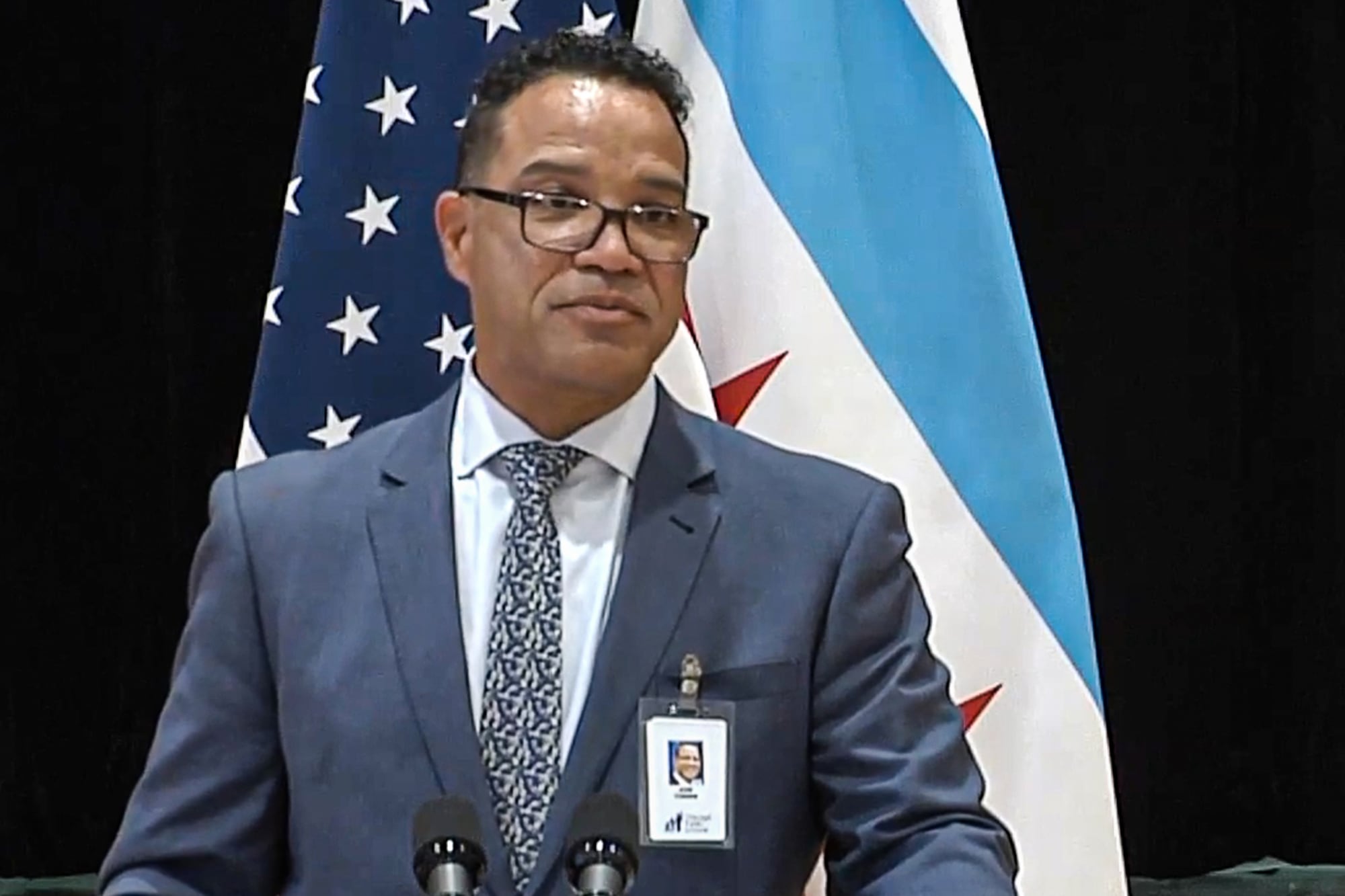Dr. José Torres speaks at a podium in front of the flags of the United States and Chicago.