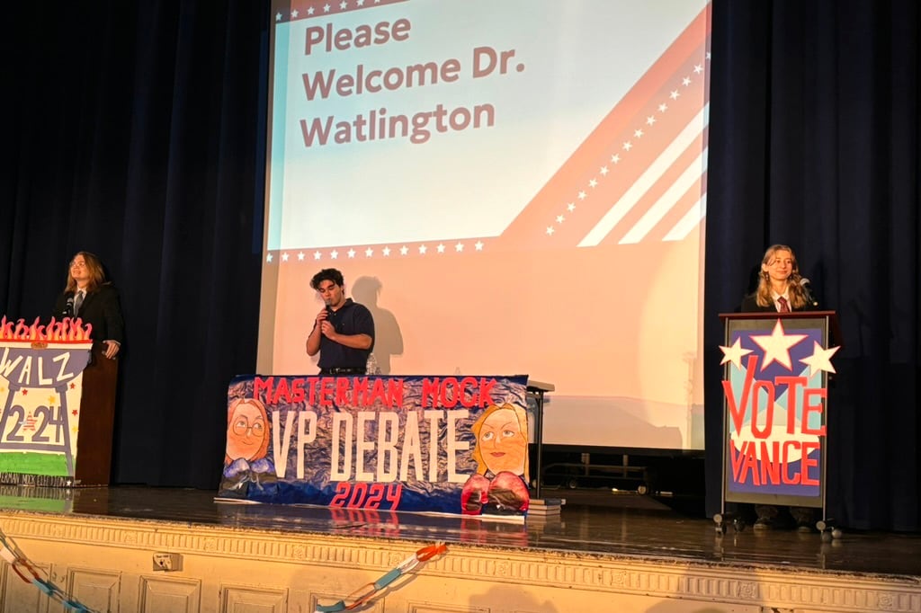 Three students stand on a mock debate stage.