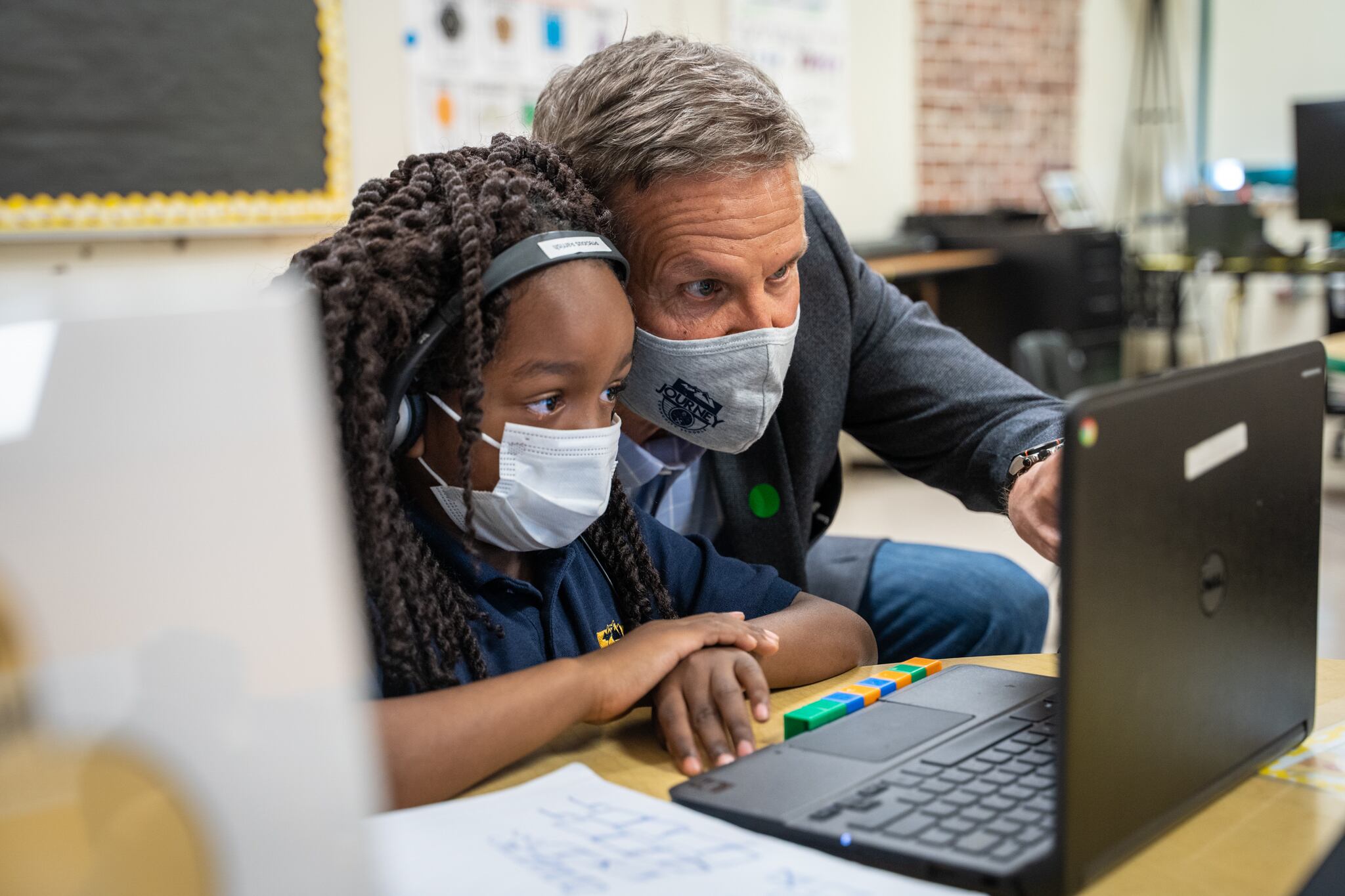 A masked man and masked girl look at a laptop screen.