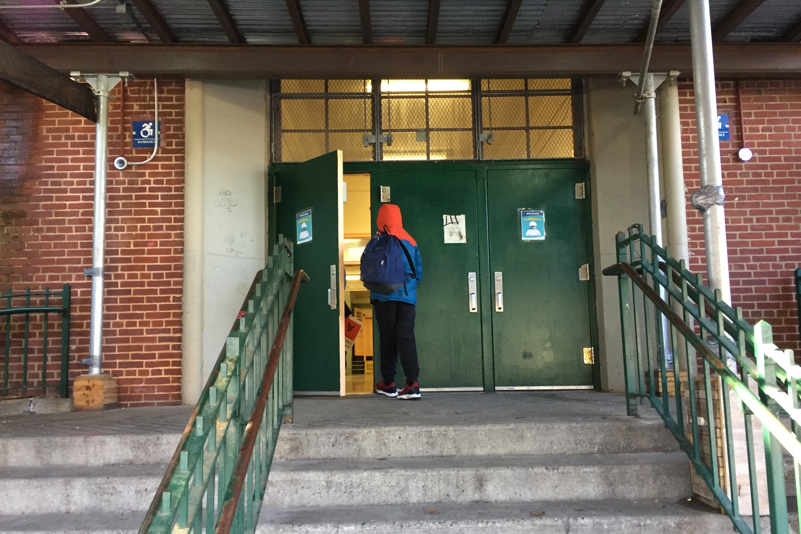 Students at M.S. 51 in Park Slope, Brooklyn walk into the building, socially distanced and masked. The foreground is steps and a green railing.