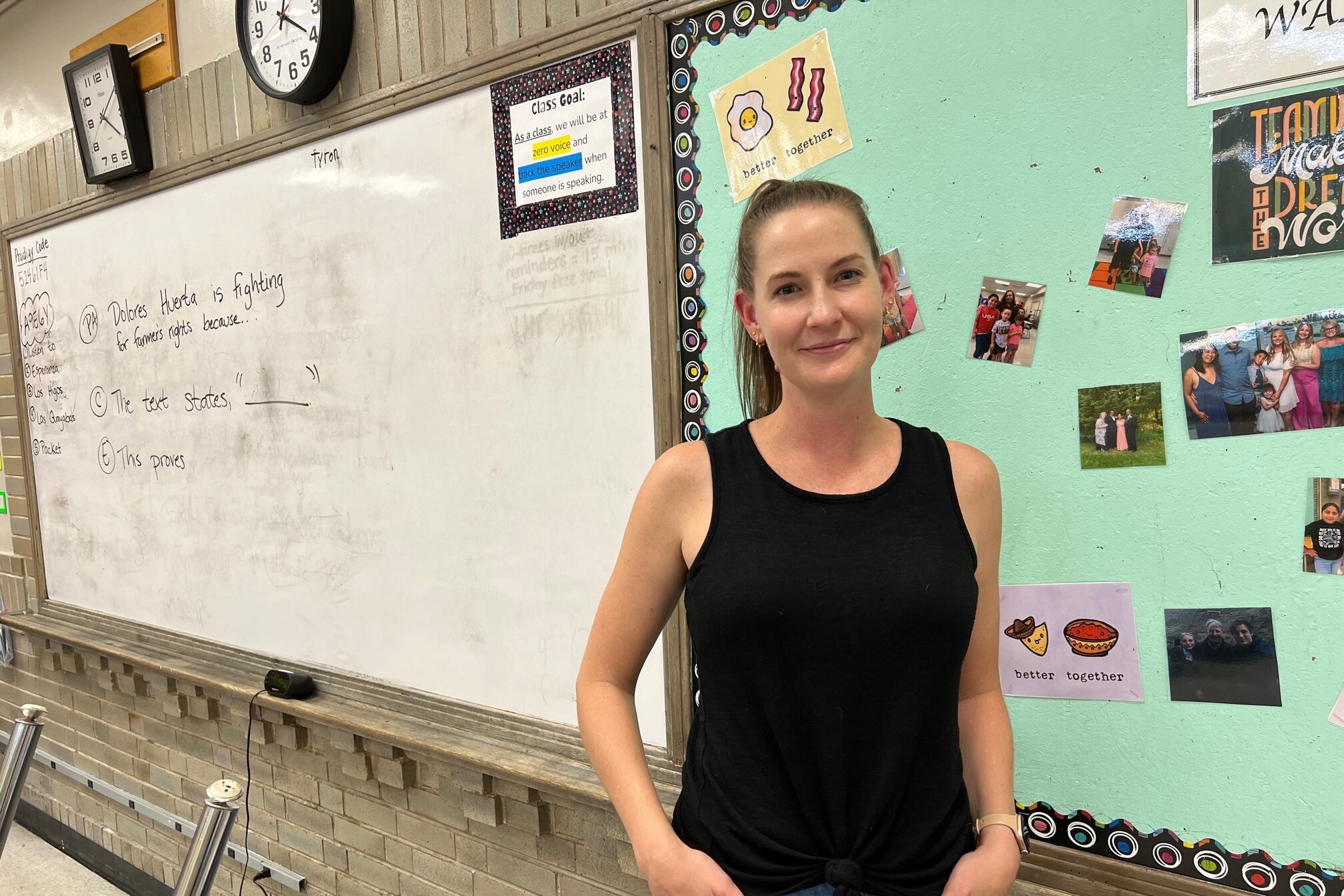 A female teacher stands in front of a bulletin board and a white board, posing for a portrait.
