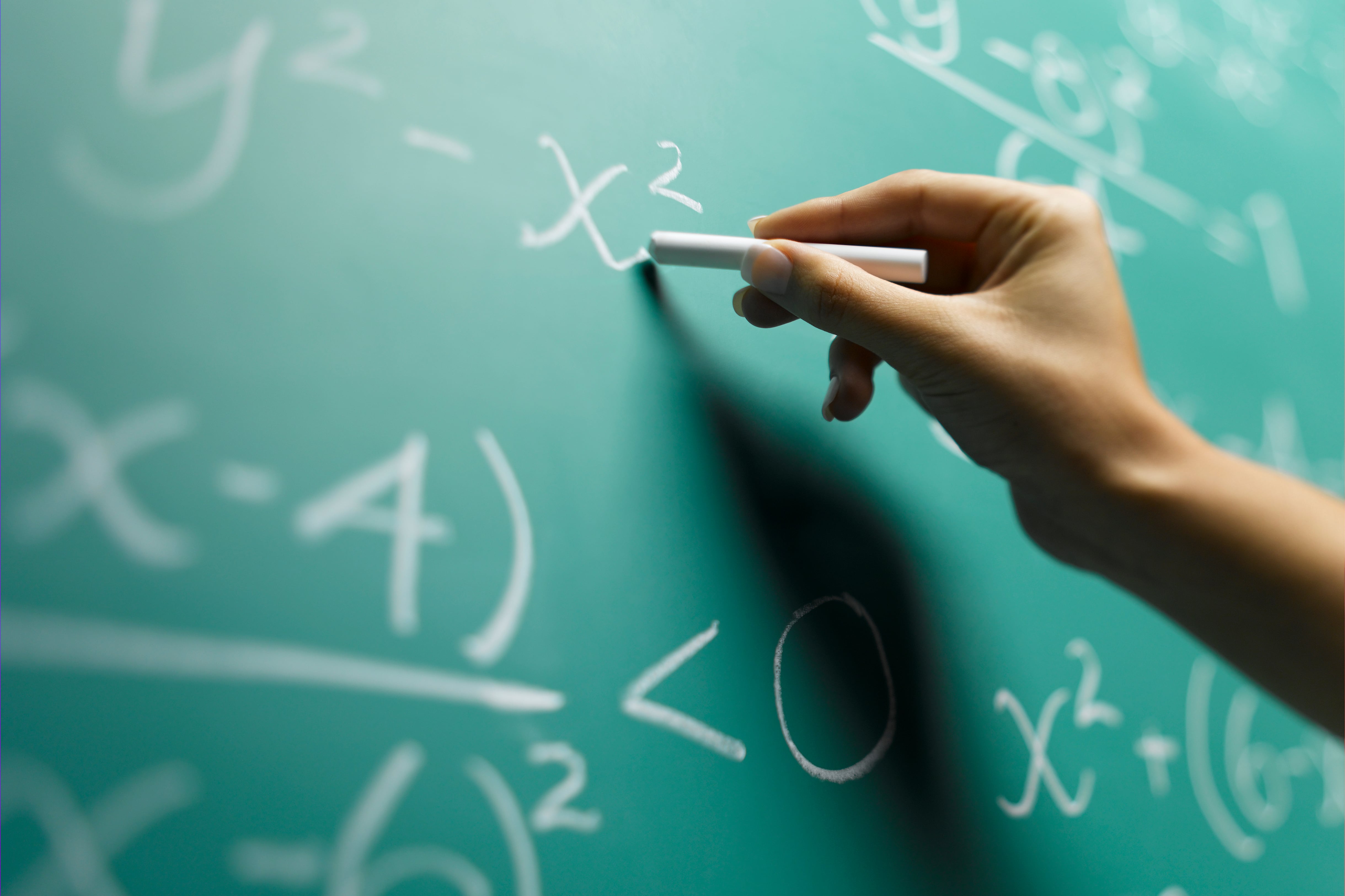 A hand holds a chalkboard and works on math.
