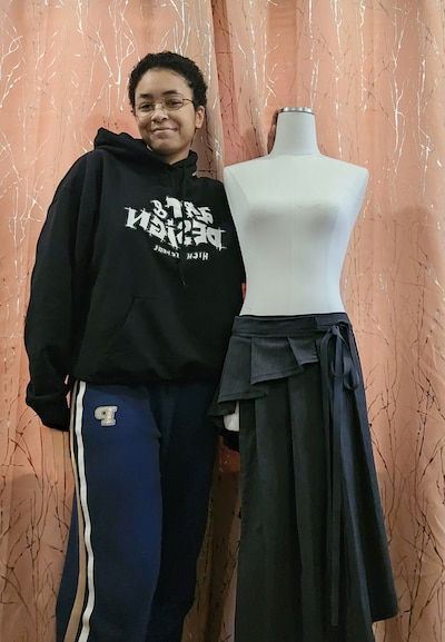 A high school student stands next to a mannequin wearing a bottom piece of clothing.