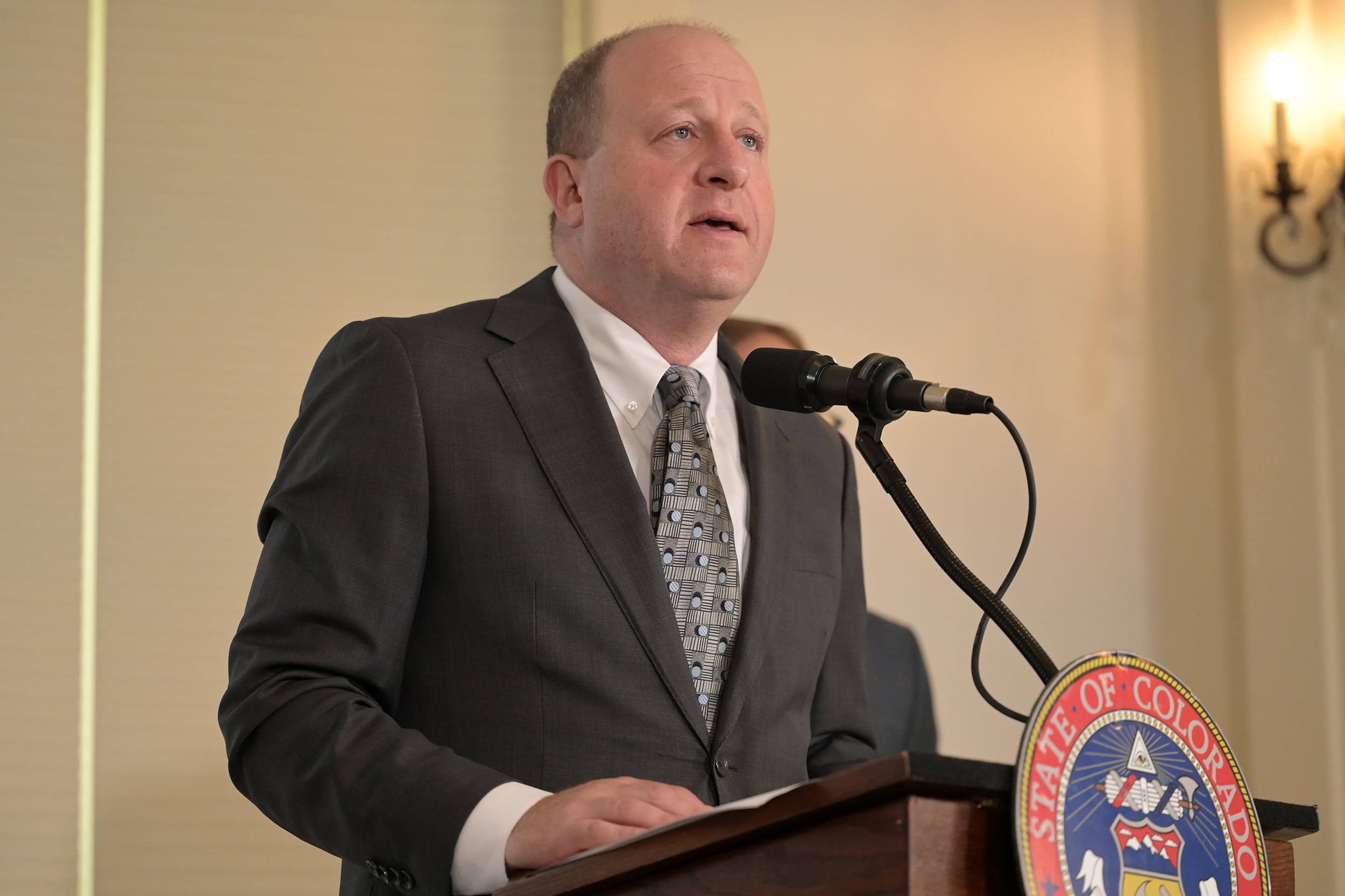 A photograph of a white man in a suit standing behind a podium giving a speech.
