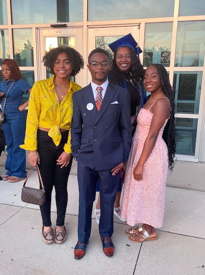 Four people stand in nice clothing posing for a portrait outside of a school.