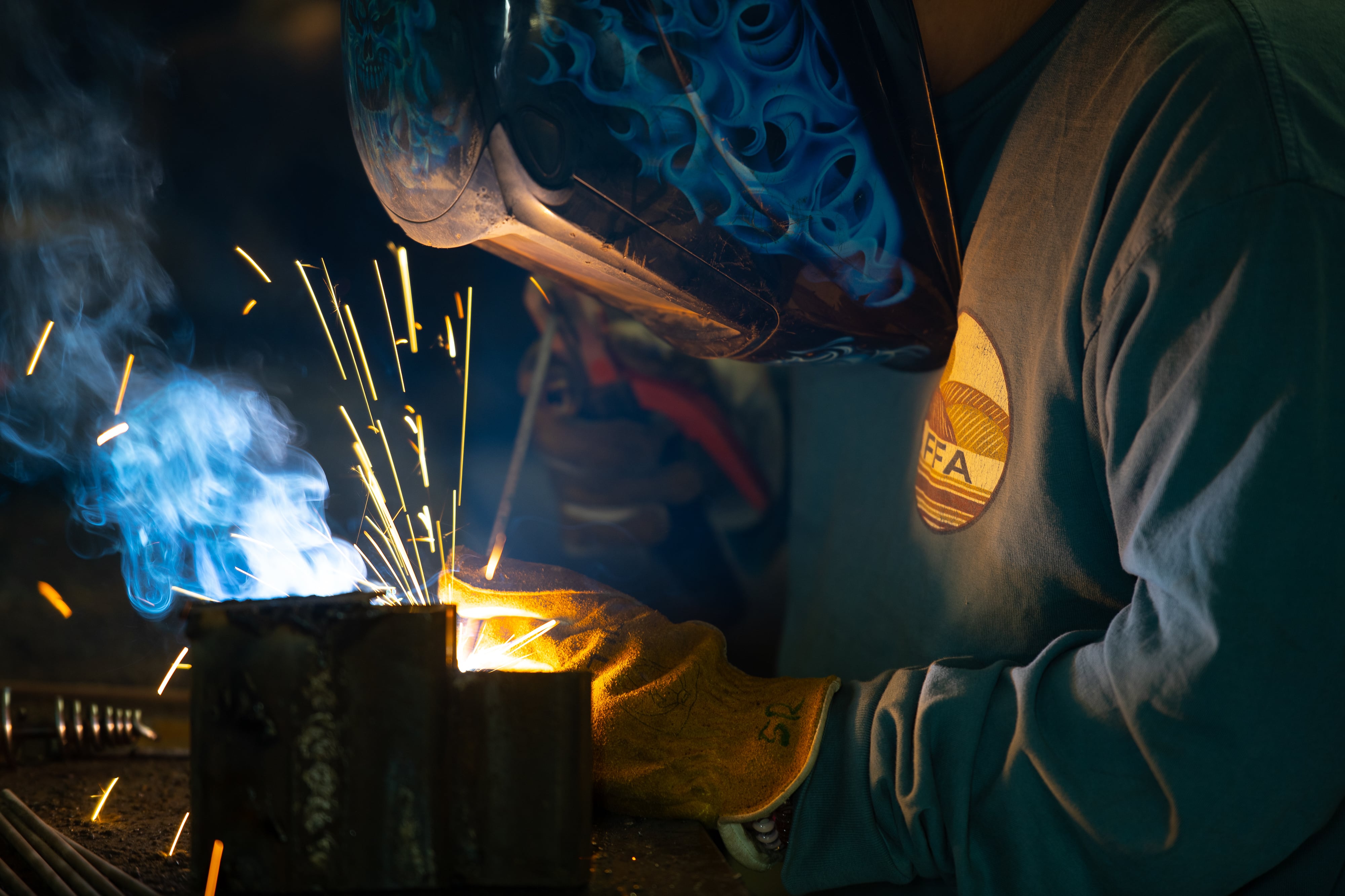 A close up of a welder working on a project with sparks flying.