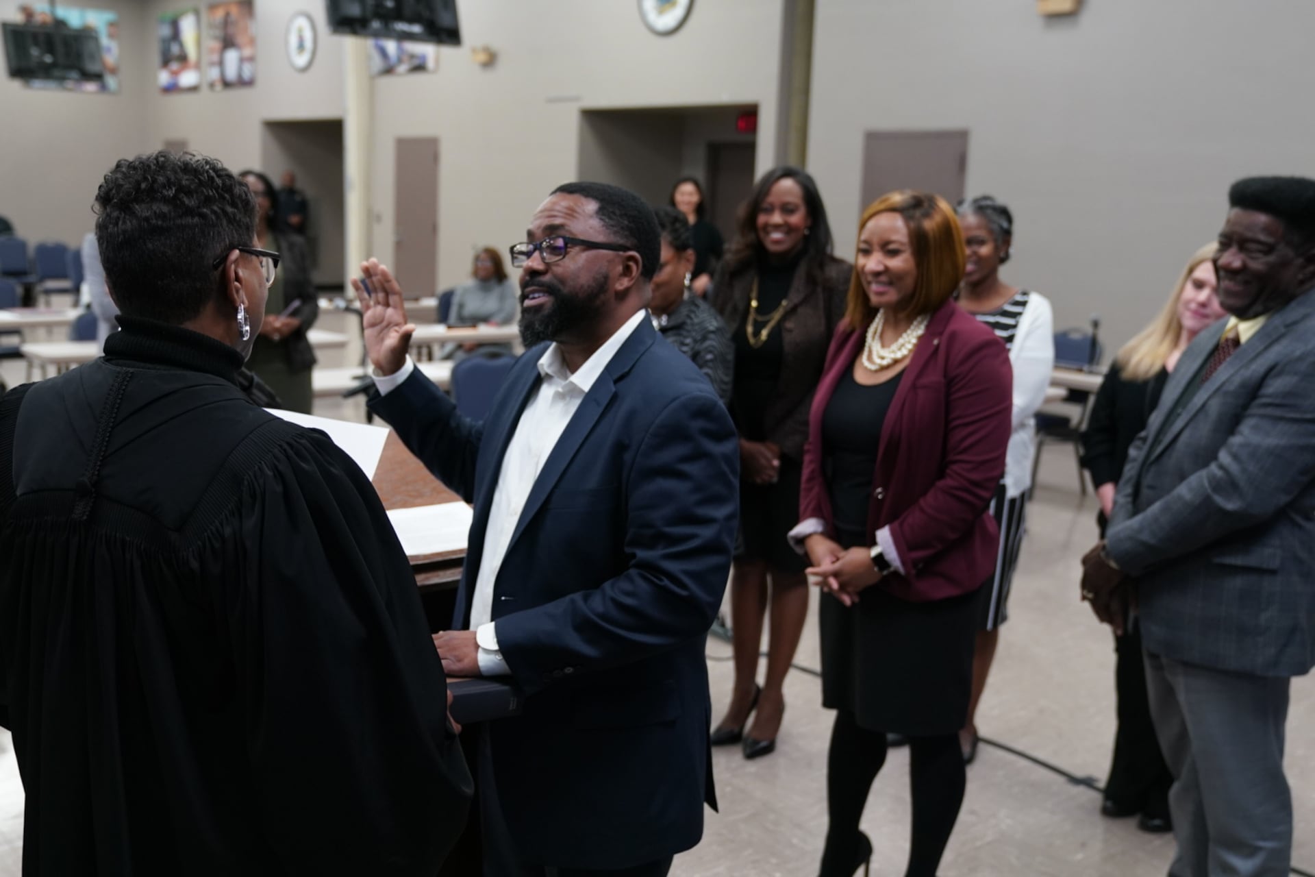 A man raises his right hand during an oath of office ceremony while a group of five other people look on smiling.