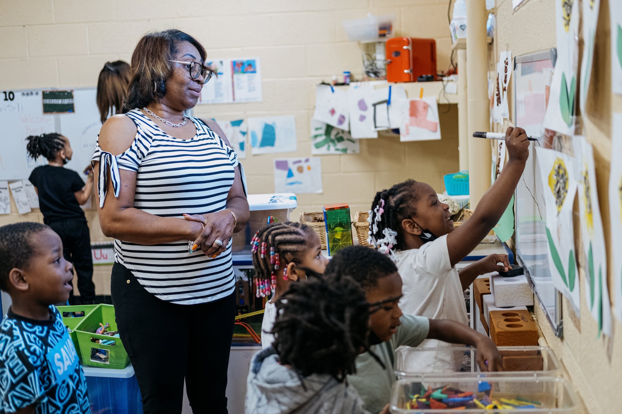 An adult watches as students draw on posters on a wall.