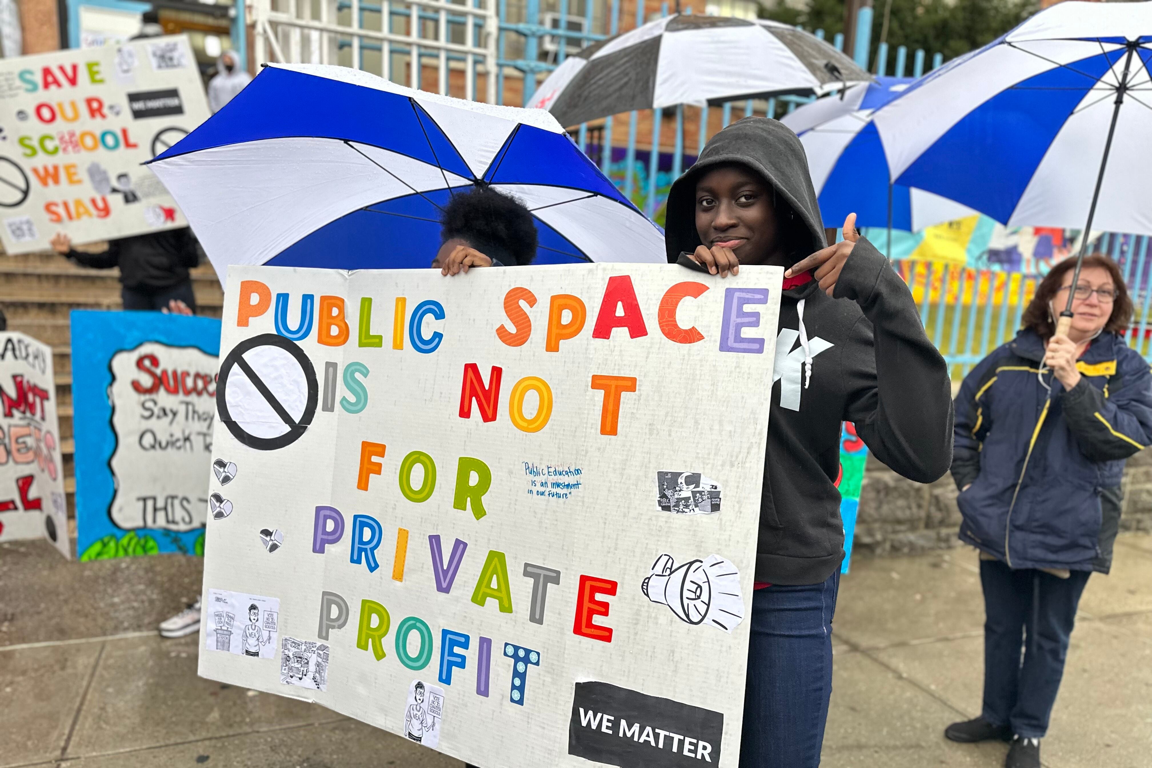 A student holds a sign saying “Public space is not for private profit.”