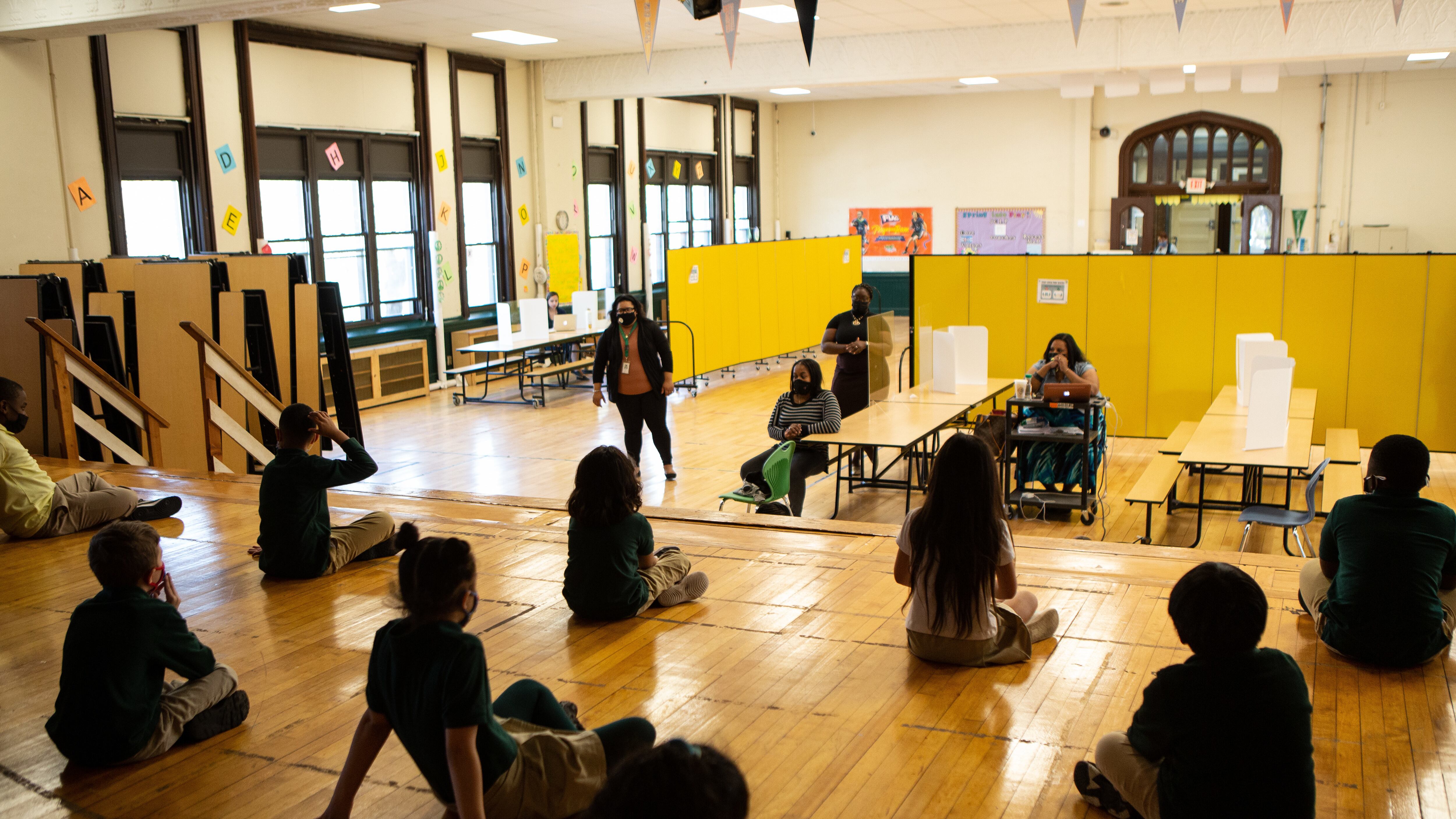 Students sit cross-legged on wood floors.