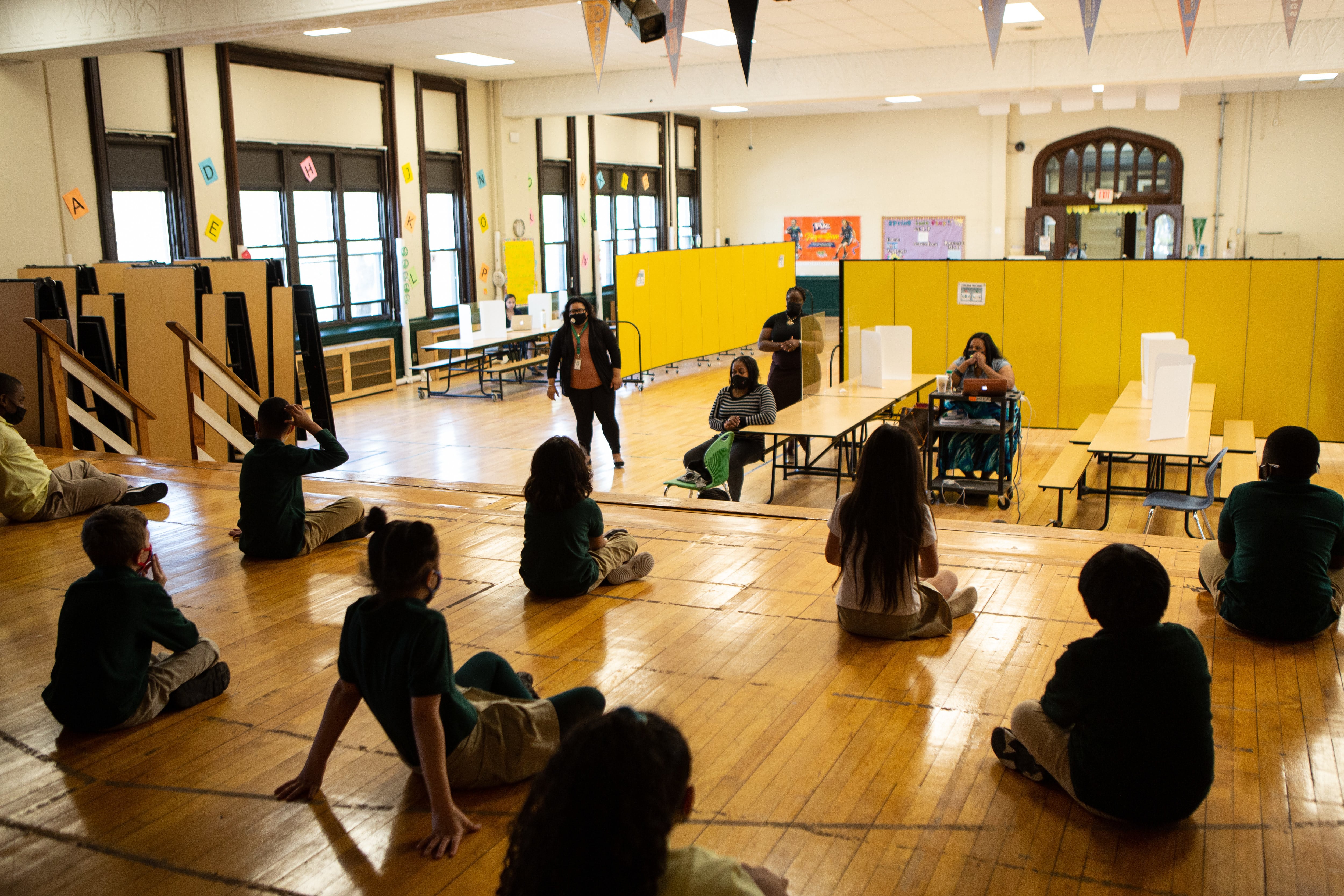 Students sit cross-legged on wood floors.