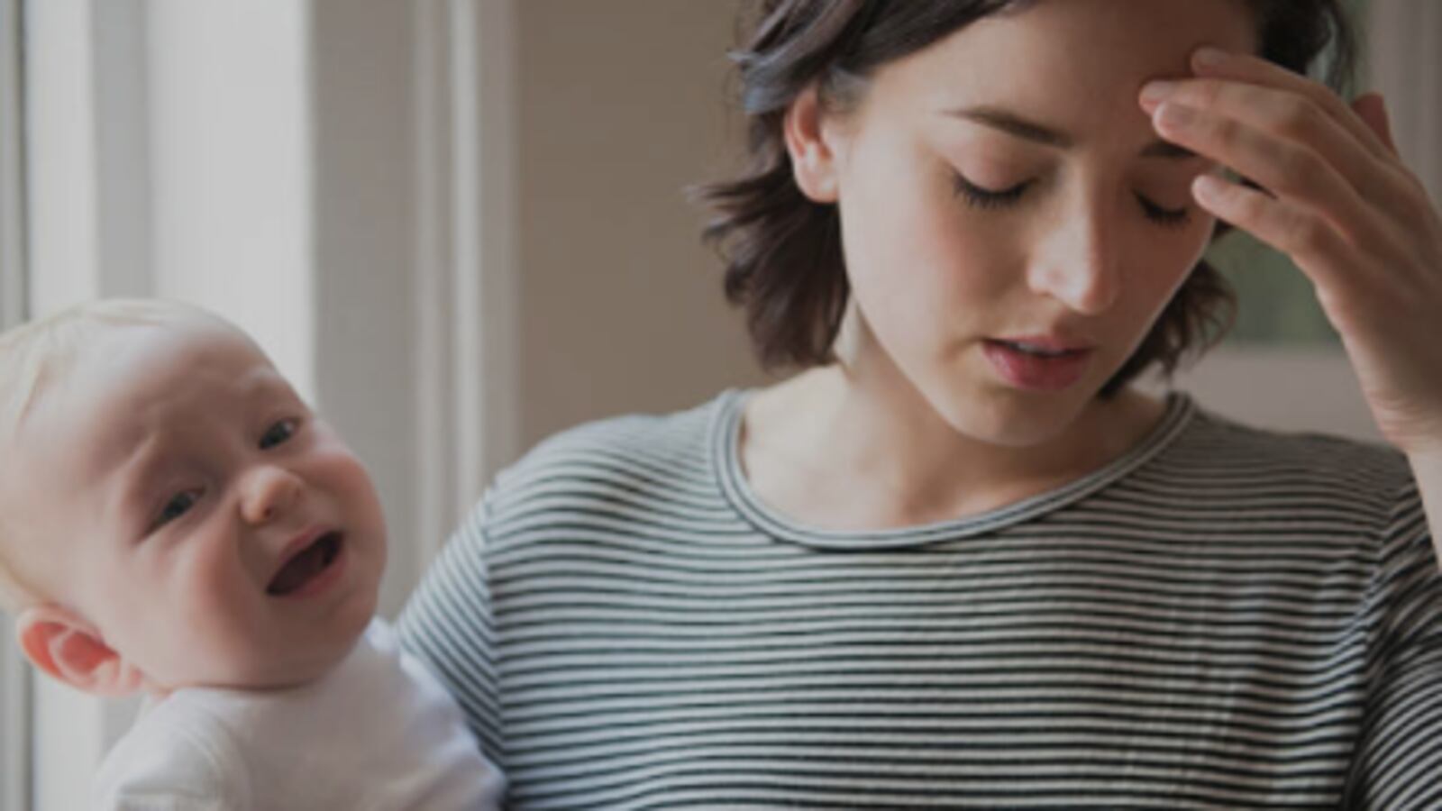 Mother rubbing forehead while holding baby son.