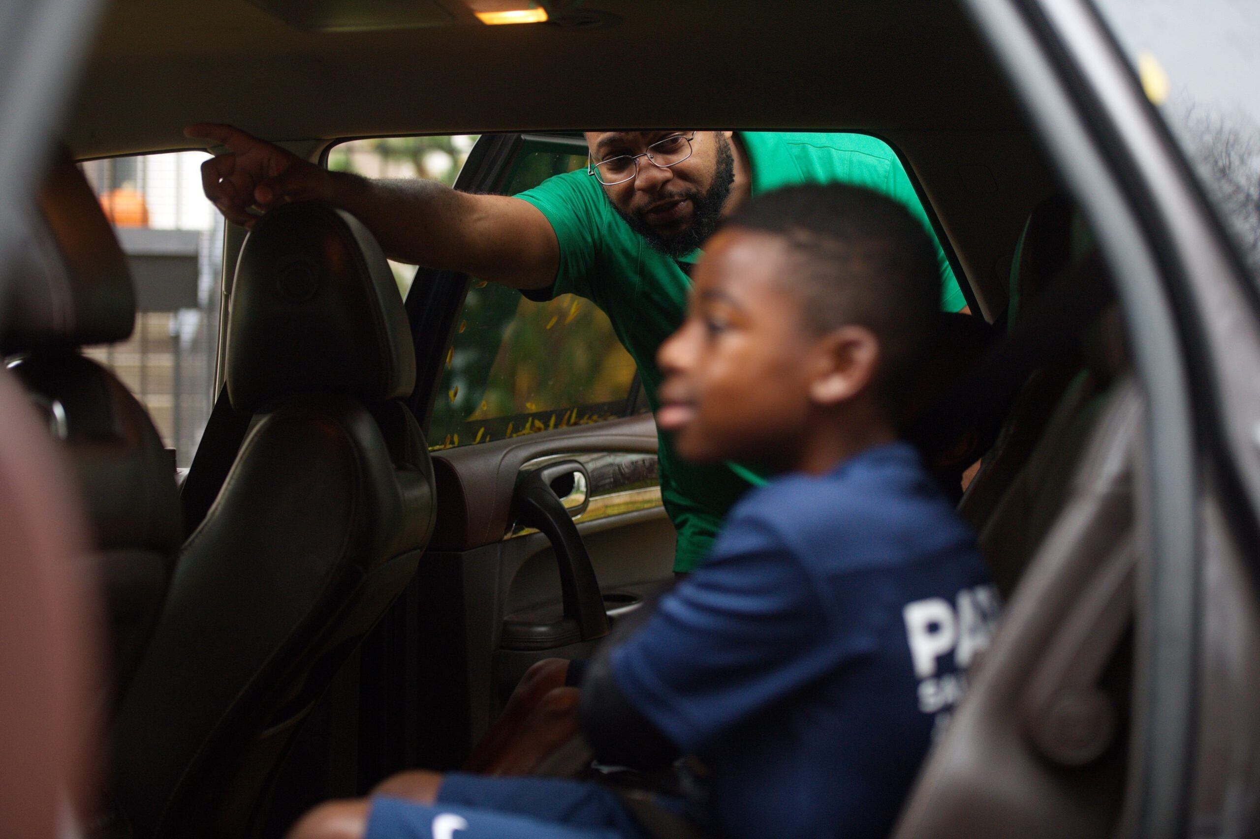 A man wearing a green shirt looks into a car with a young boy in the foreground.