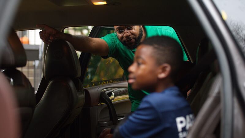 A man wearing a green shirt looks into a car with a young boy in the foreground.