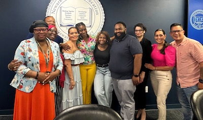 A woman in a brightly-colored blouse and yellow pants poses for a photo with a group of other people.