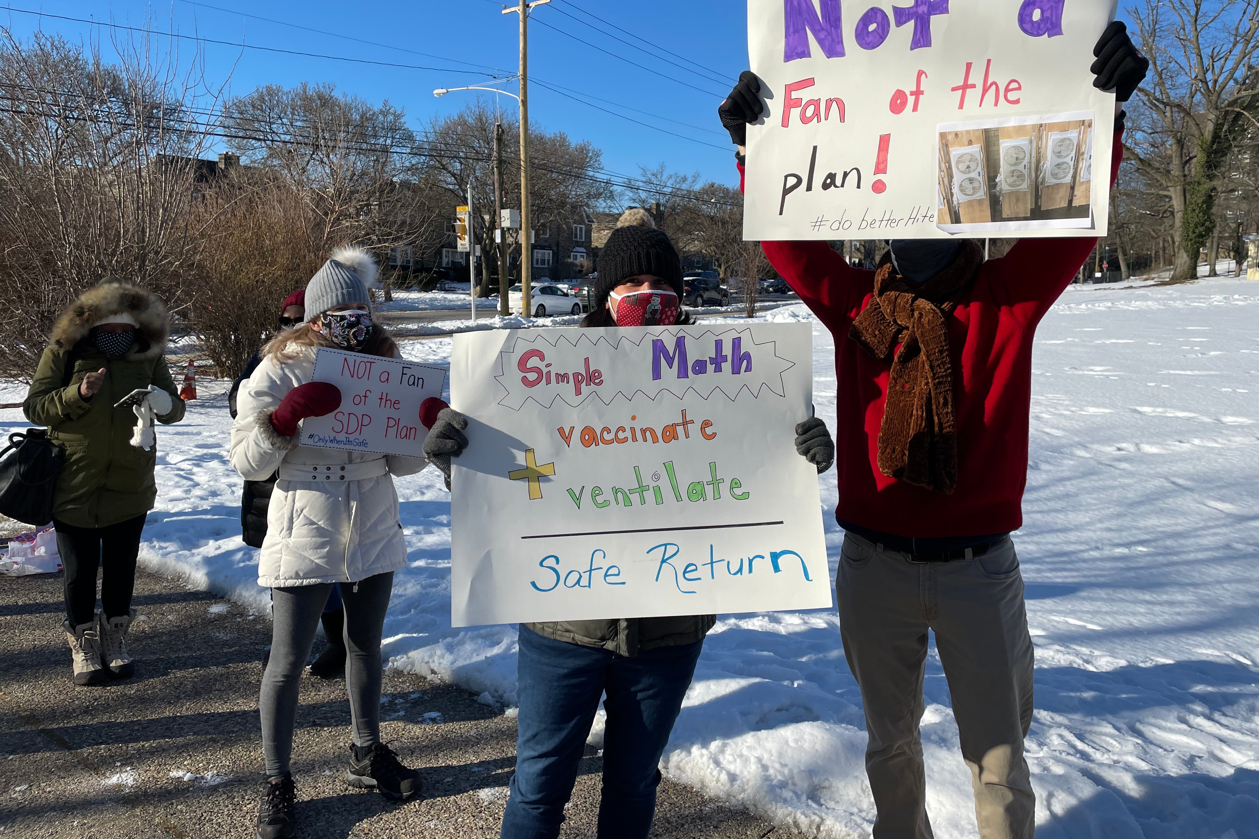 Teachers holding posters that read: "Not a fan of the plan!" and "Simple math: vaccinate + ventilate = safe return."