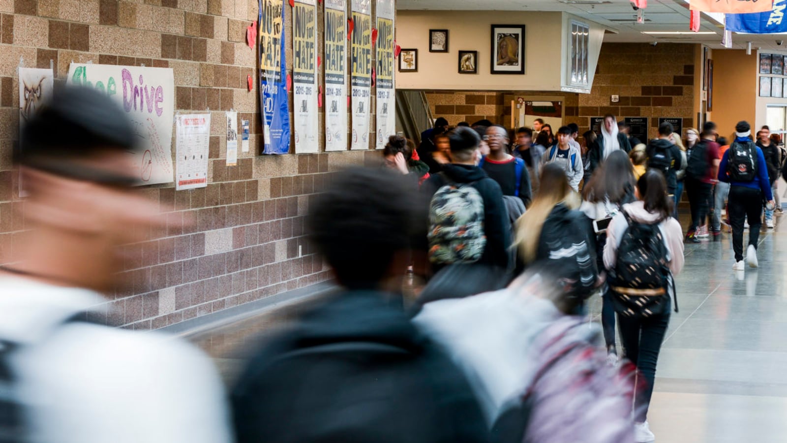 The backs of students as they walk through a hall at Adams City High School