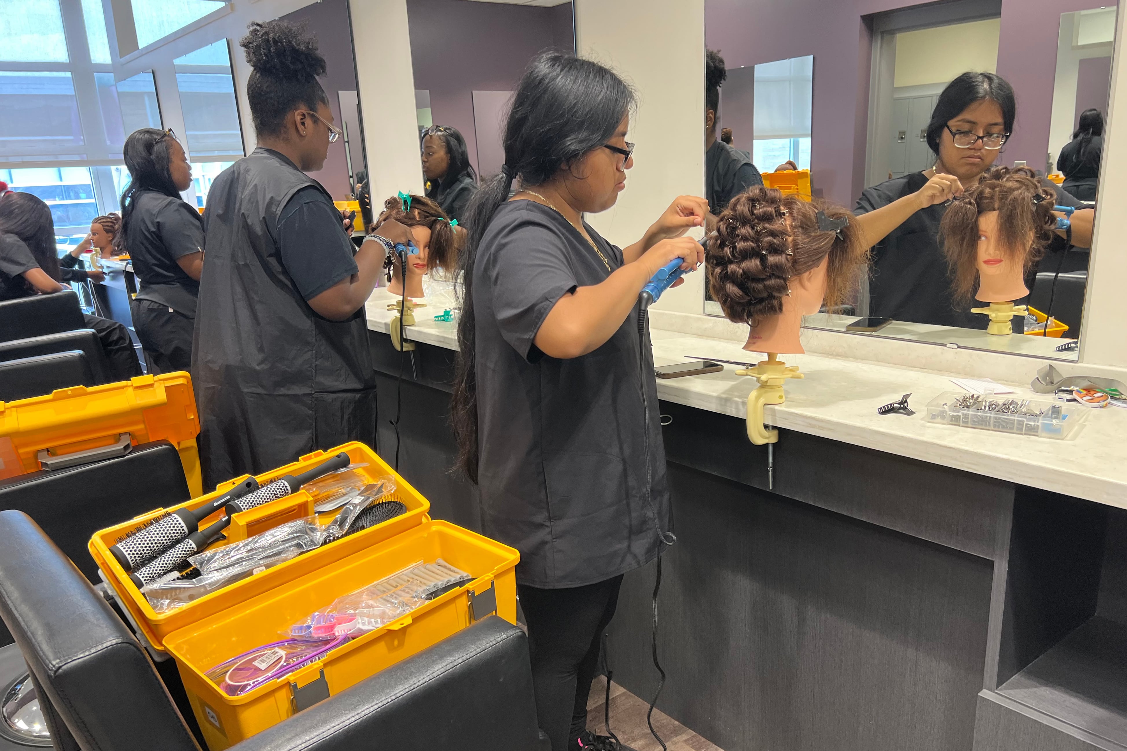 Four cosmetology students at their work stations practice curling hair on mannequins.