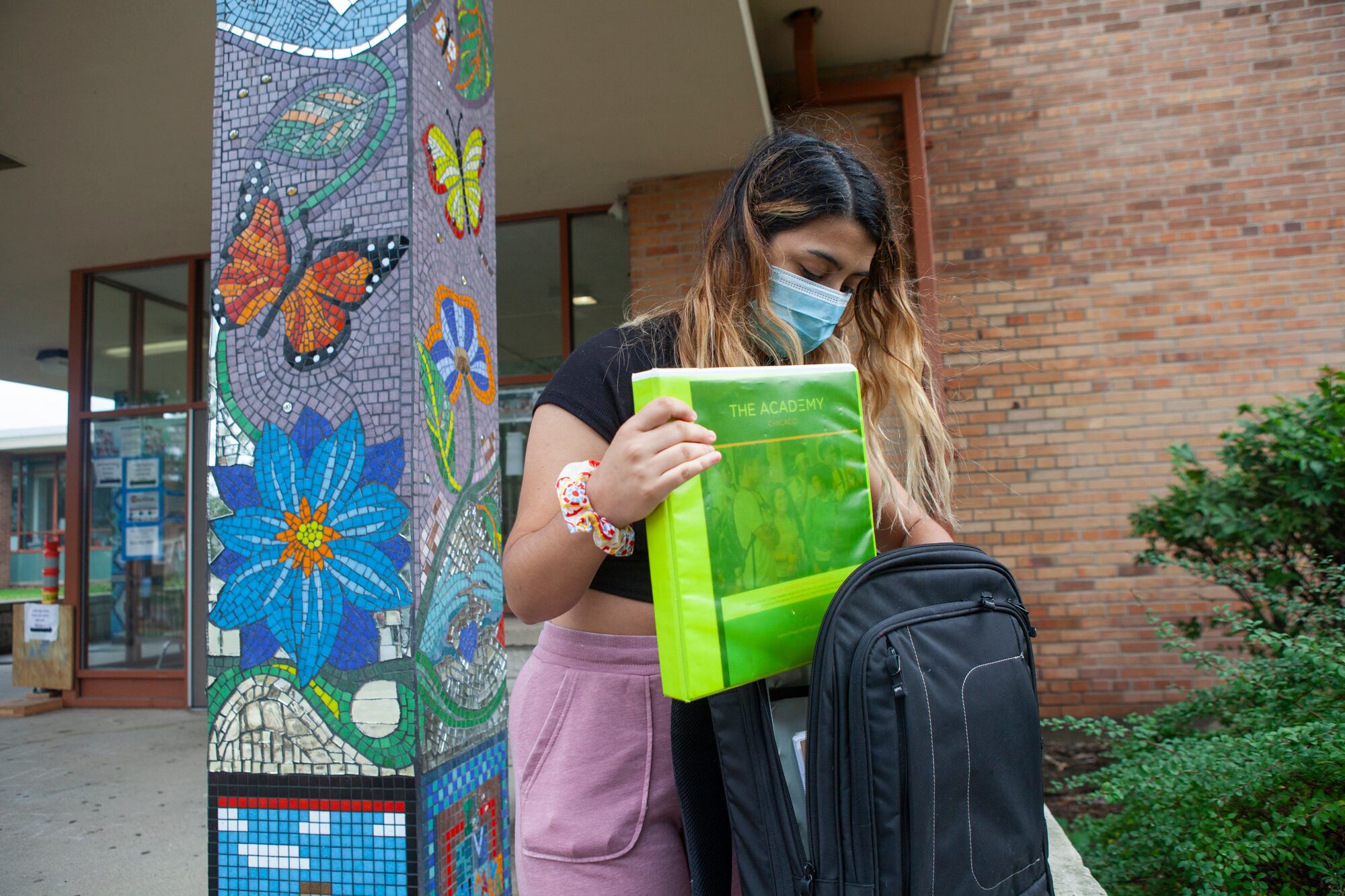 Trinity putting a green binder into her backpack.
