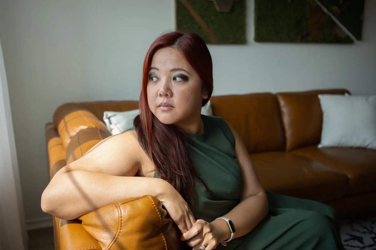 A woman sits on a leather couch, hands clasped and looking over her shoulder.