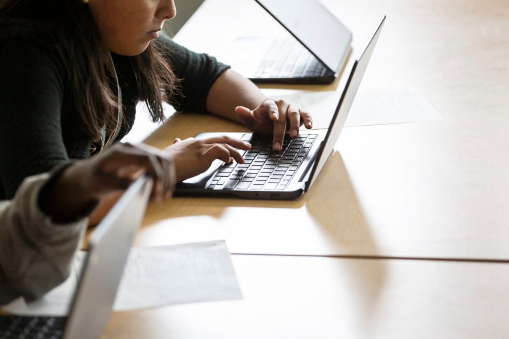 A young student works on a laptop on a wooden table.
