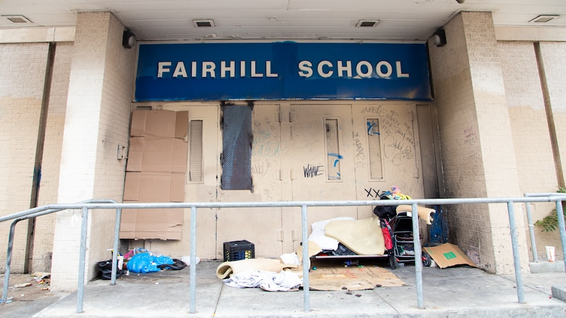 a photograph of the outside of an abandoned school with a blue sign with white letters that reads "Fairhill School."