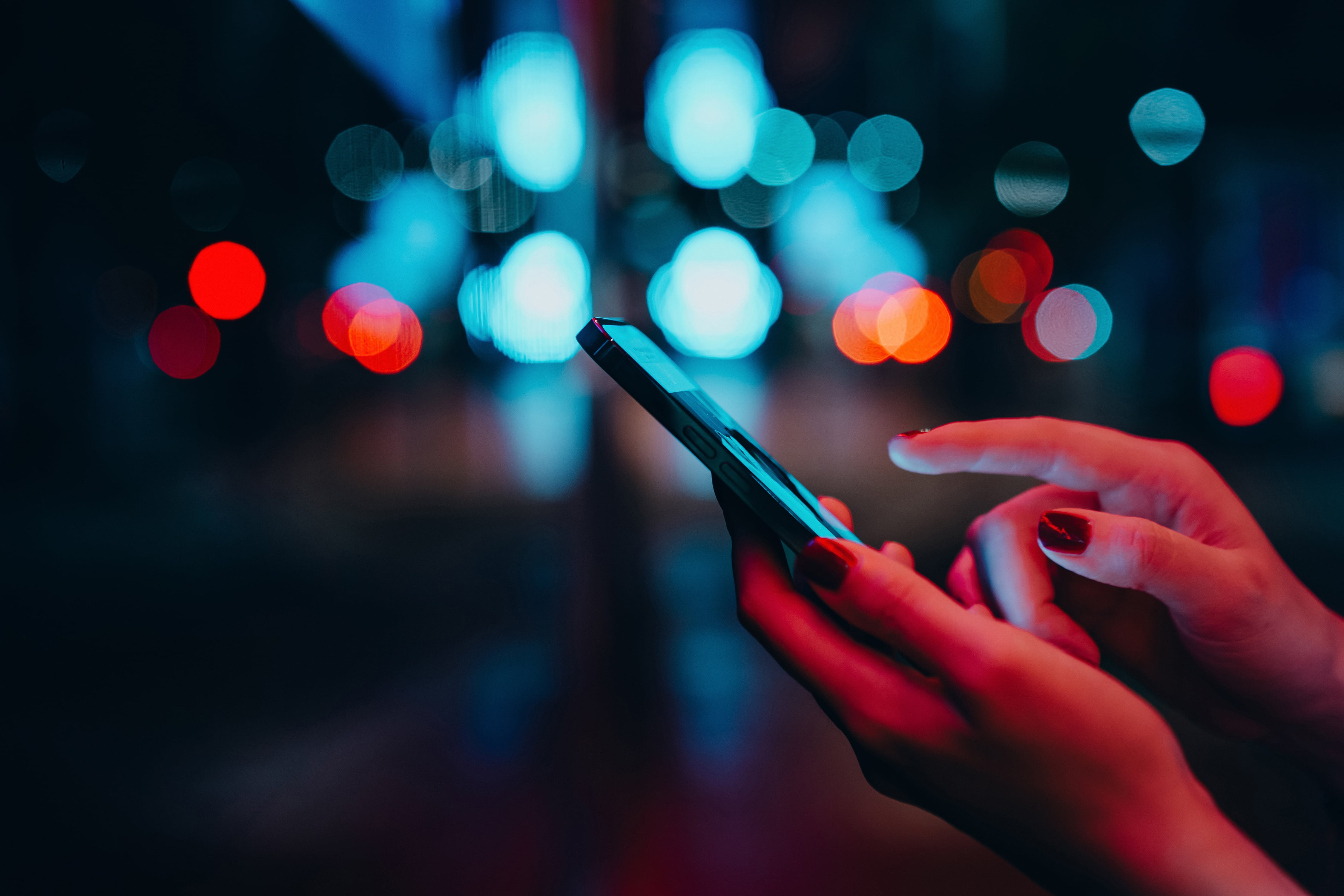 A woman uses a cell phone with street lights in the background.