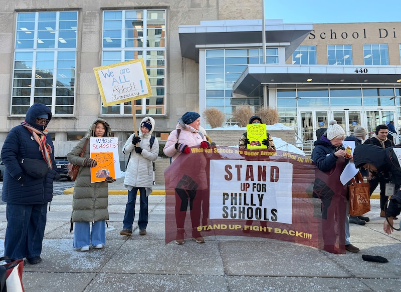 A photograph of a group of people wearing large winter coats and signs protesting outside of a large building.