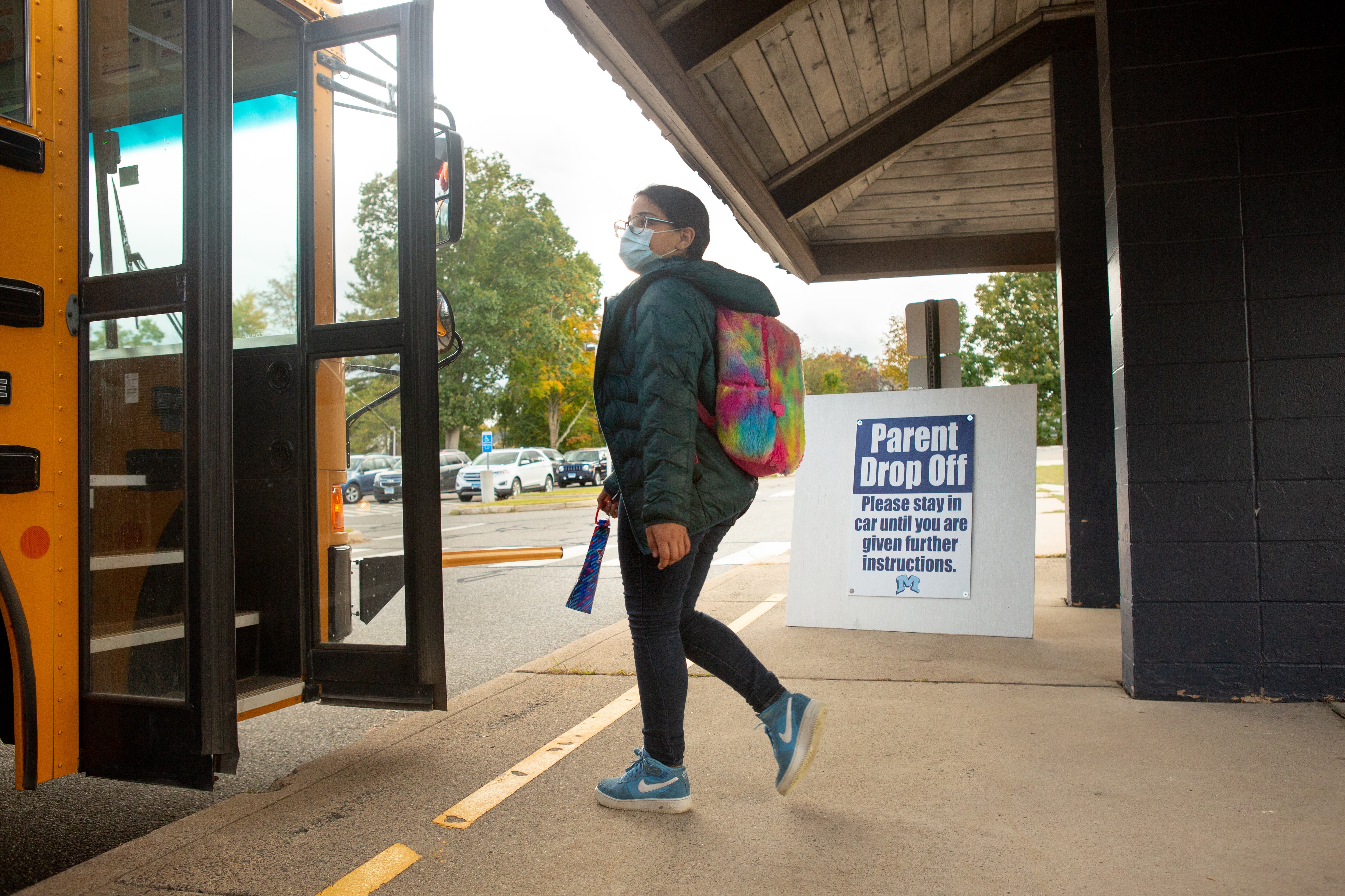 A student carrying a multicolored backpack boards a school bus after dismissal.