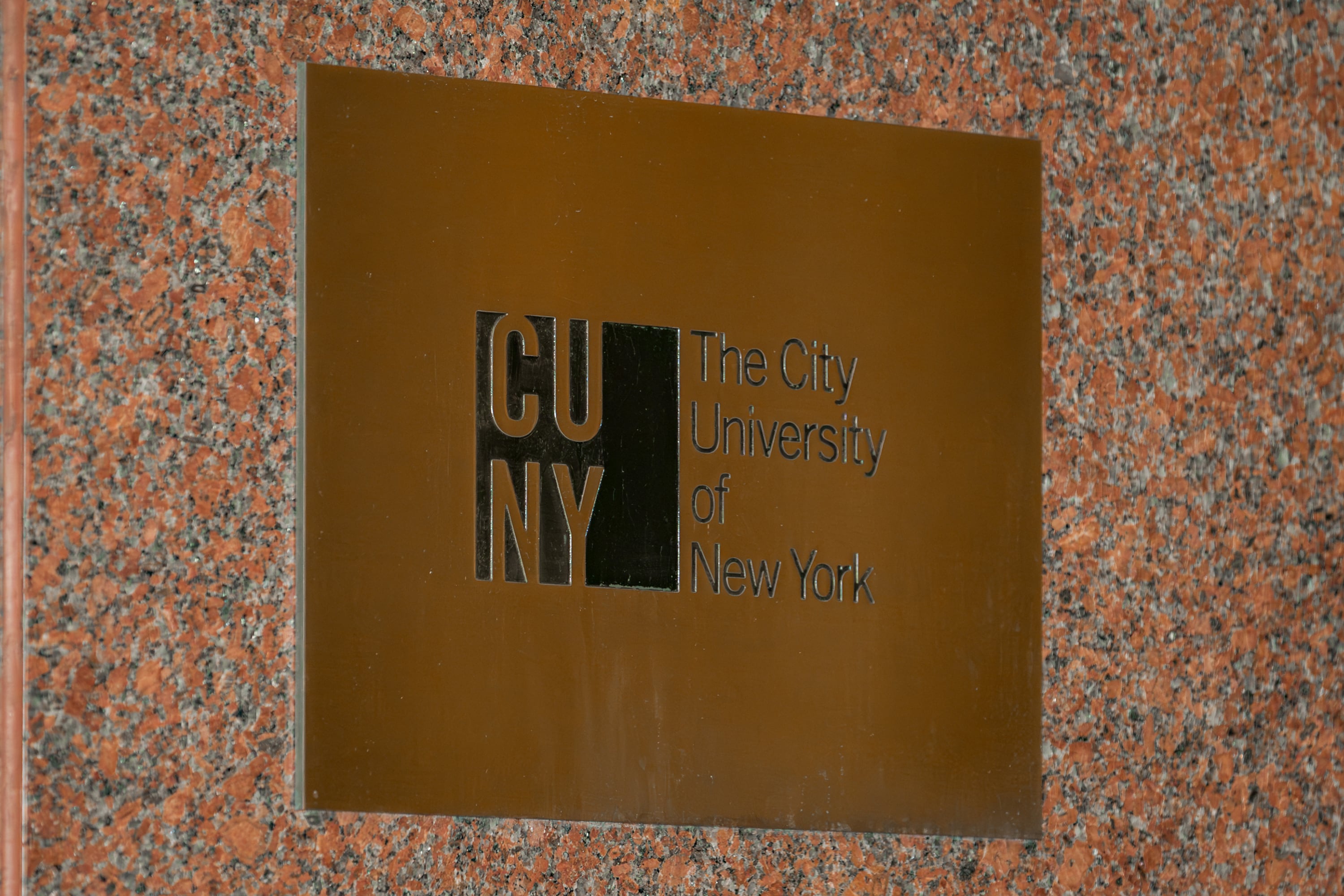 A photograph of a gold plaque with the words " CUNY The City University of New York."