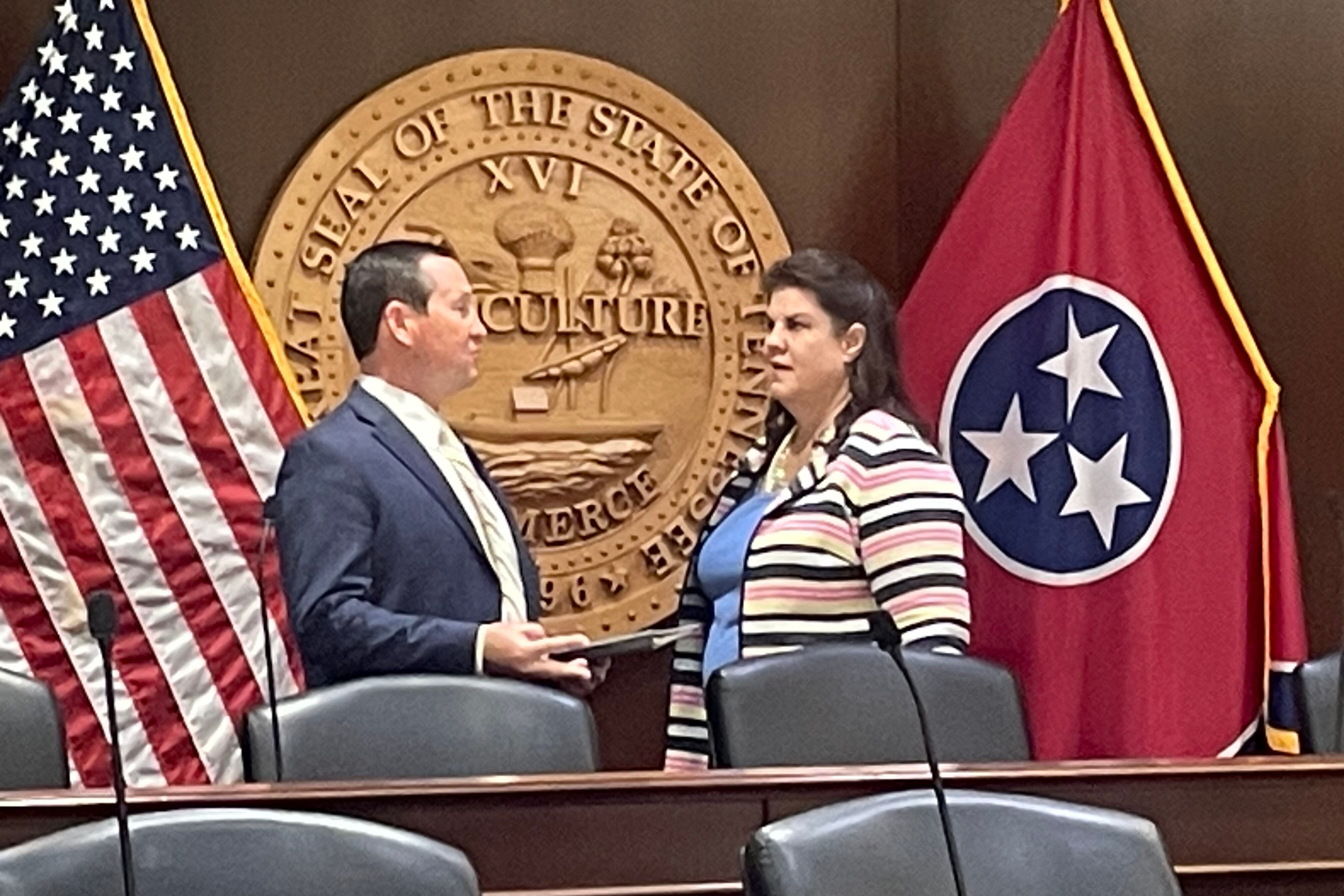 Two people stand in front of Tennessee state seal and two flags.