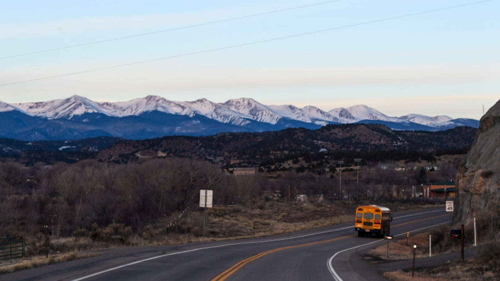 A school bus from the Primero district drives down a highway with the Sangre de Cristo mountains in the background.