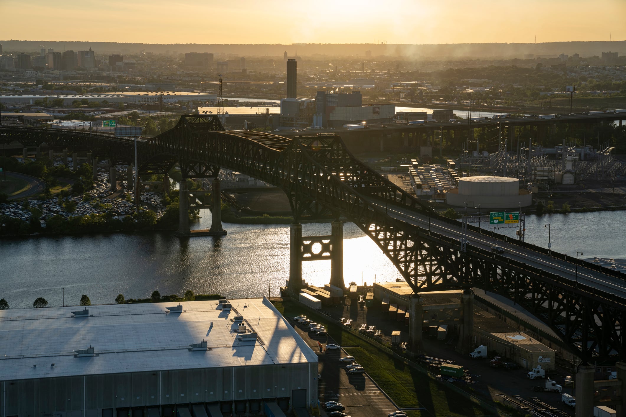 Aerial photo of the Pulaski Skyway bridge connecting Newark and Jersey City at sunset. The photo captures the bridge and surrounding buildings as the sunset is reflecting off of the Hackensack river.