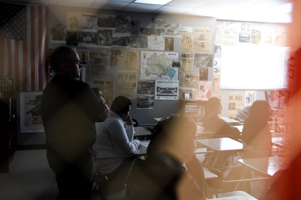 A shadowed teacher stands at the back of the class in front of students.