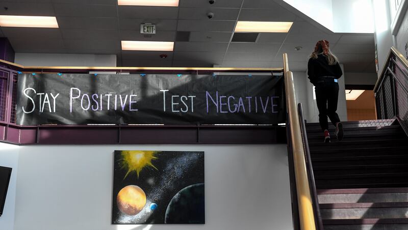 A large banner hangs from a railing at the top of the stairs in a high school. It reads, “Stay positive, test negative.”