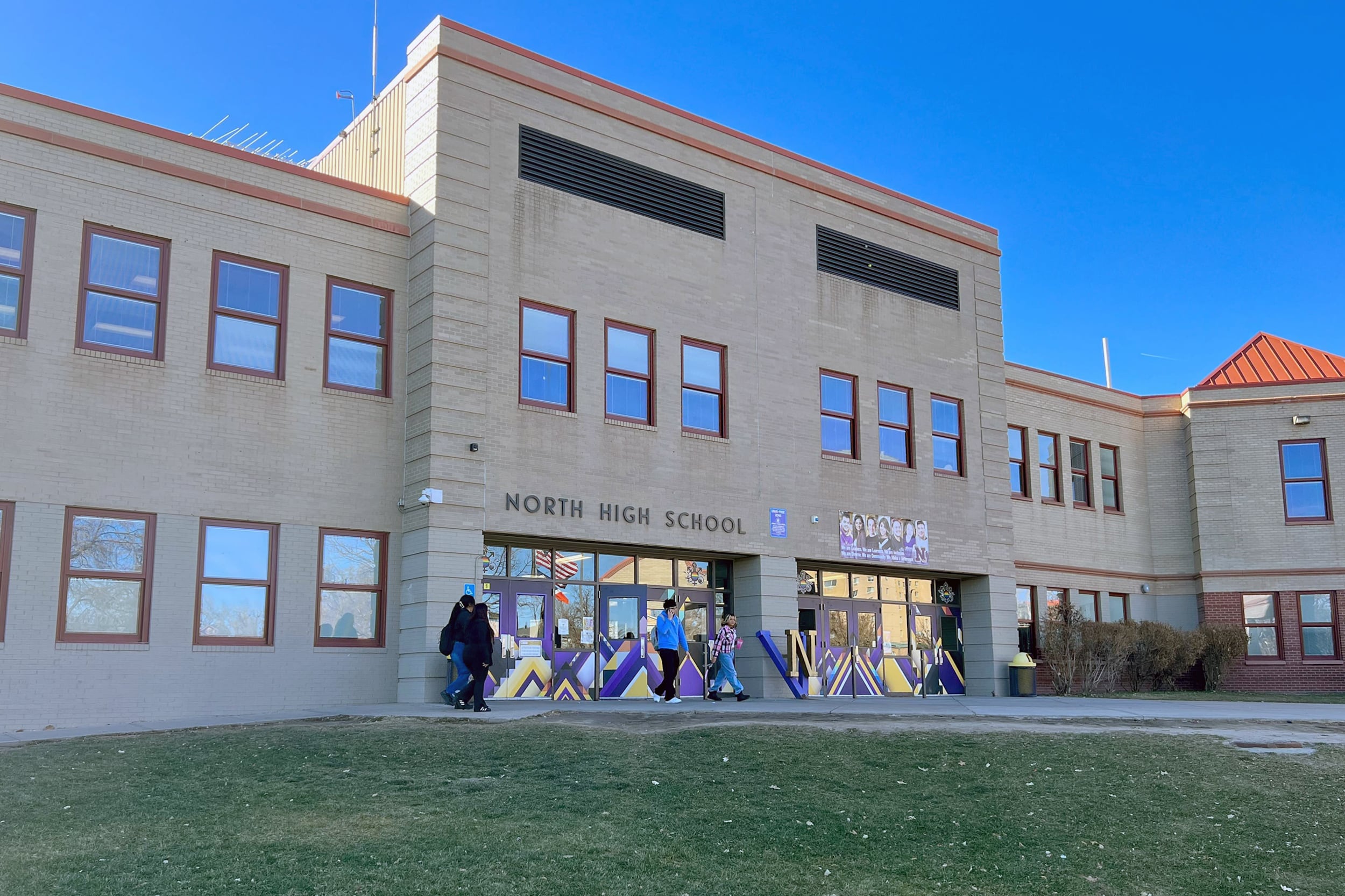 A large tan brick building with students near the front entrance.